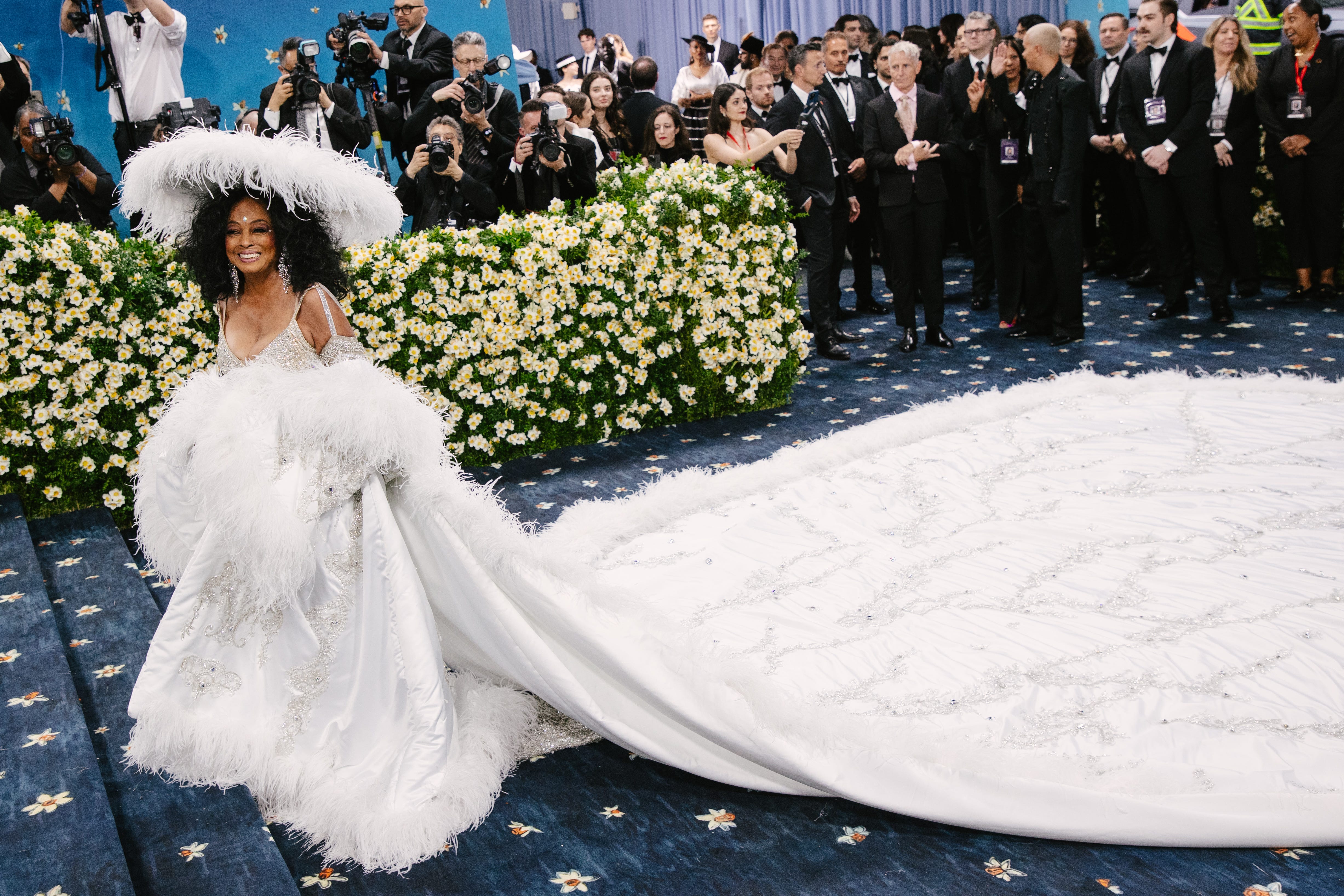 Diana Ross walks the Met Gala red carpet in a white outfit with feather detailing and a massive train.
