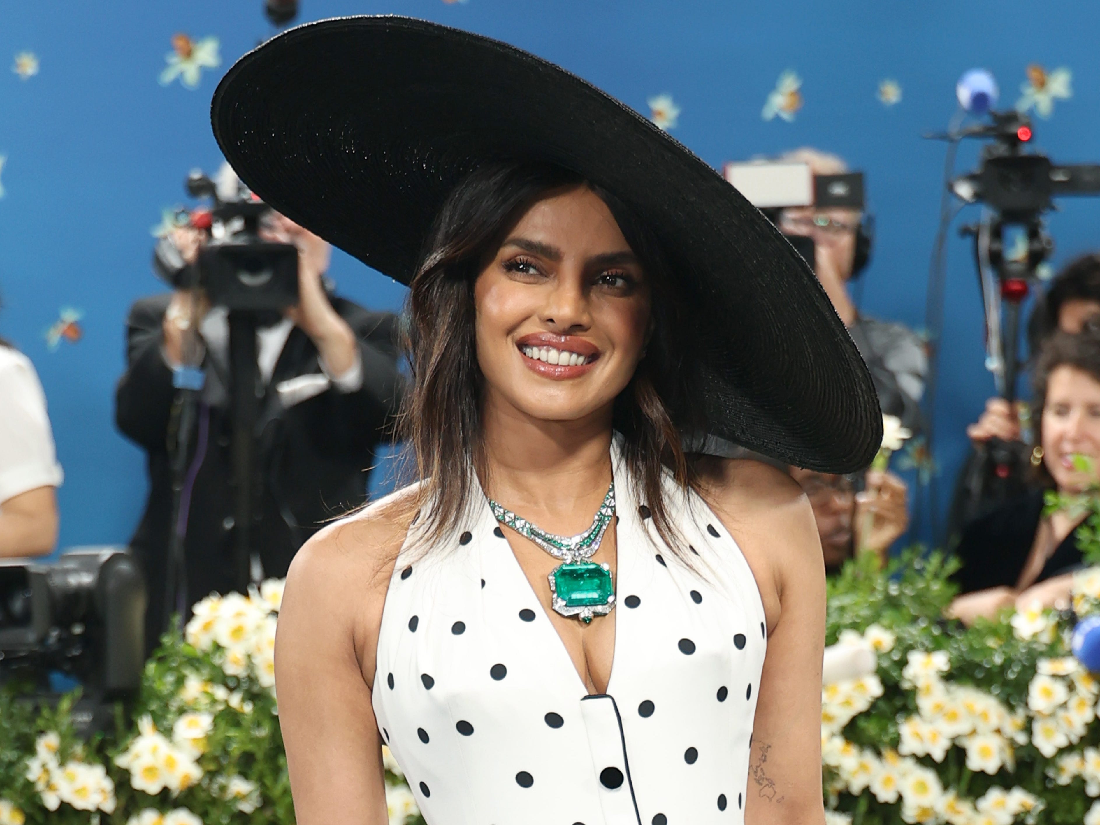 Priyanka Chopra Jonas wears a black hat, giant emerald necklace, and a polka dot dress at the met gala.