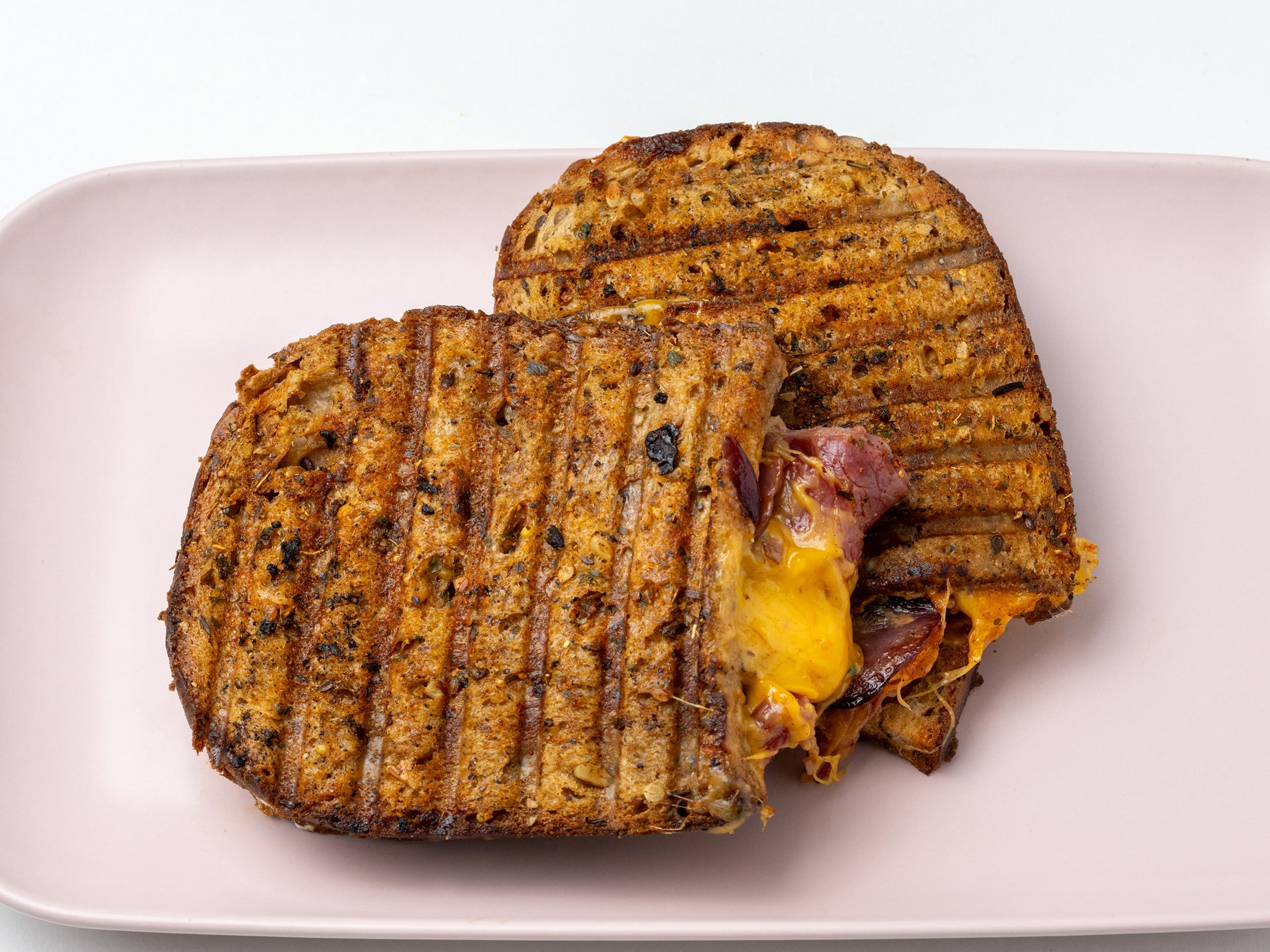 Grilled cheese on rounded bread with bacon and cheese oozing out on pink plate