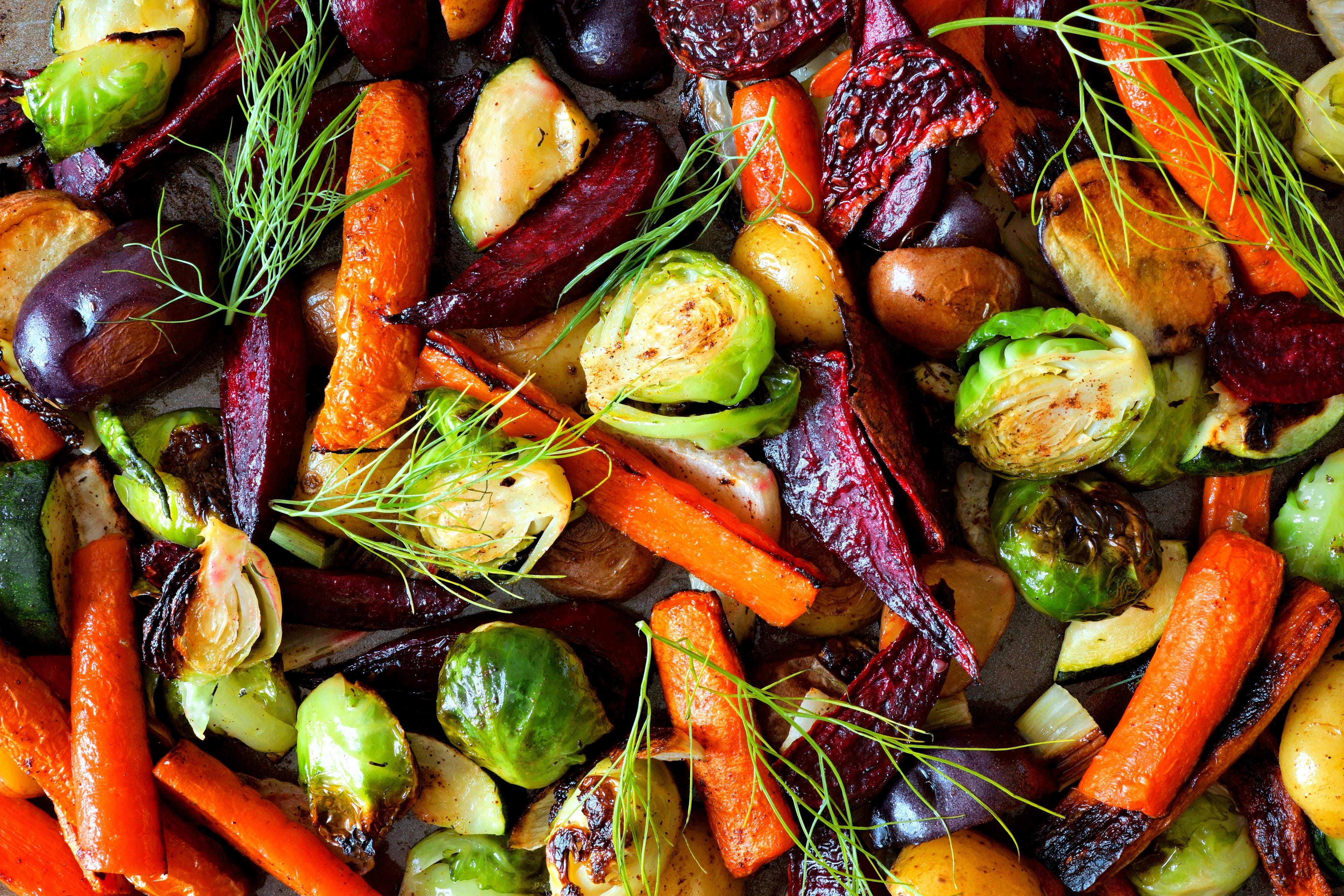 Roasted vegetables like beets, carrots, and Brussels sprouts on a pan.