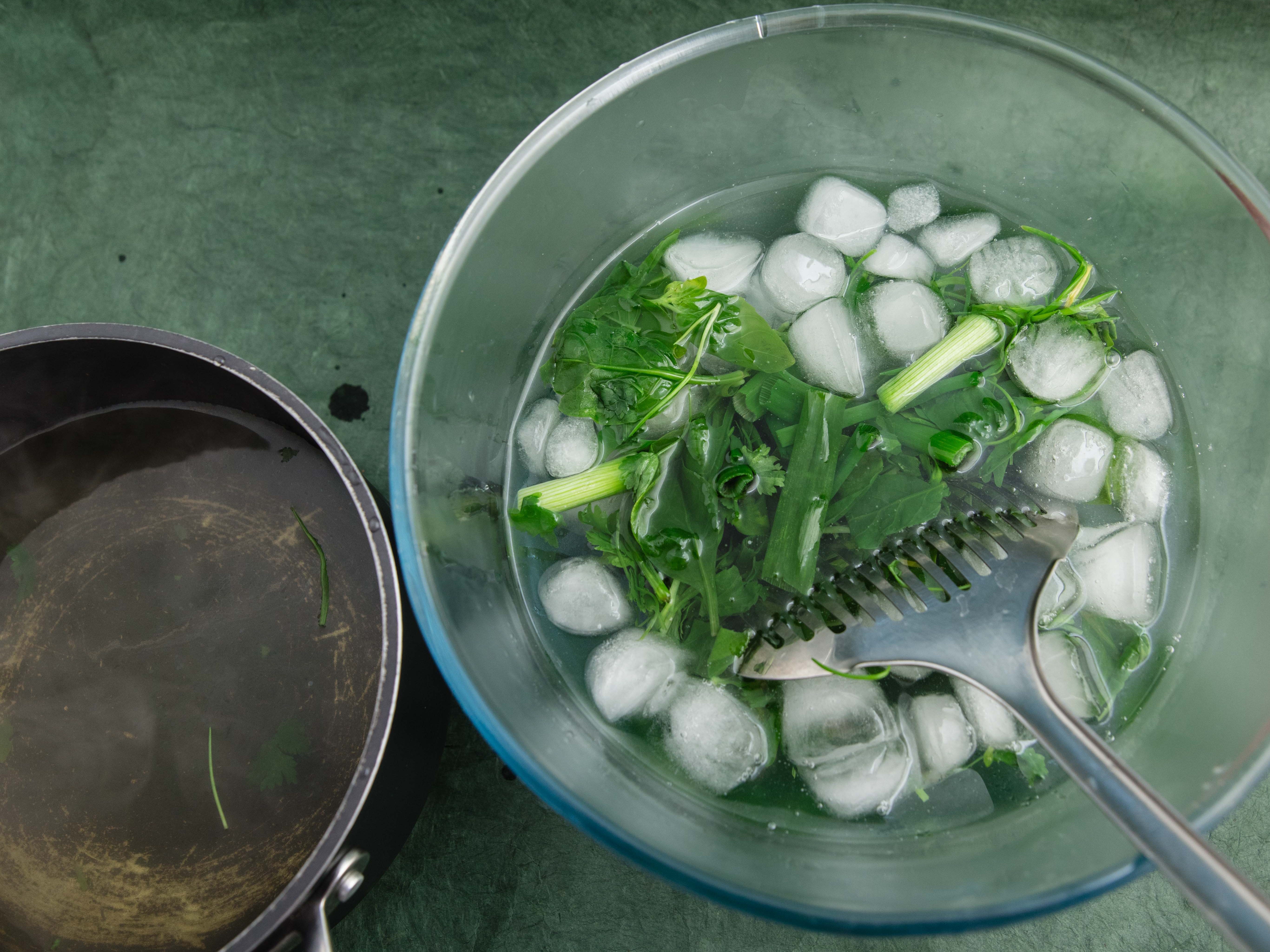 Ice-water bath with greens in it being moved by metal spoon