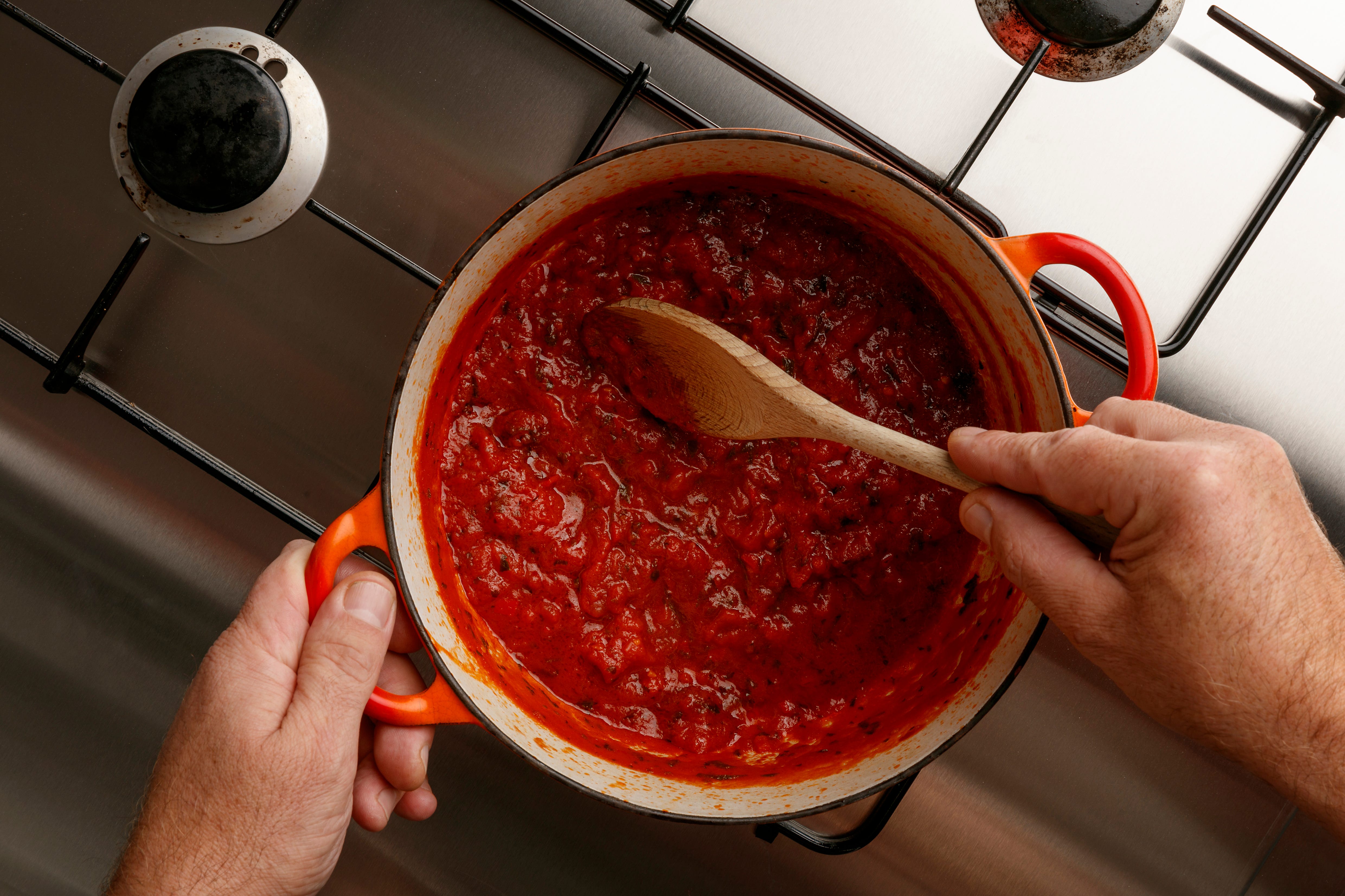 Hands stirring sauce with wooden spoon on stovetop