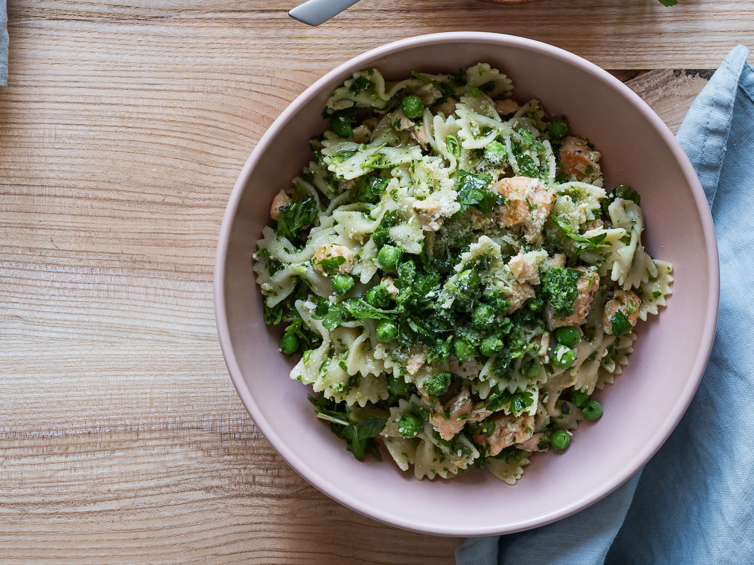 Bowl of bowtie pasta with pesto on it next to bowl of pesto with spoon in it