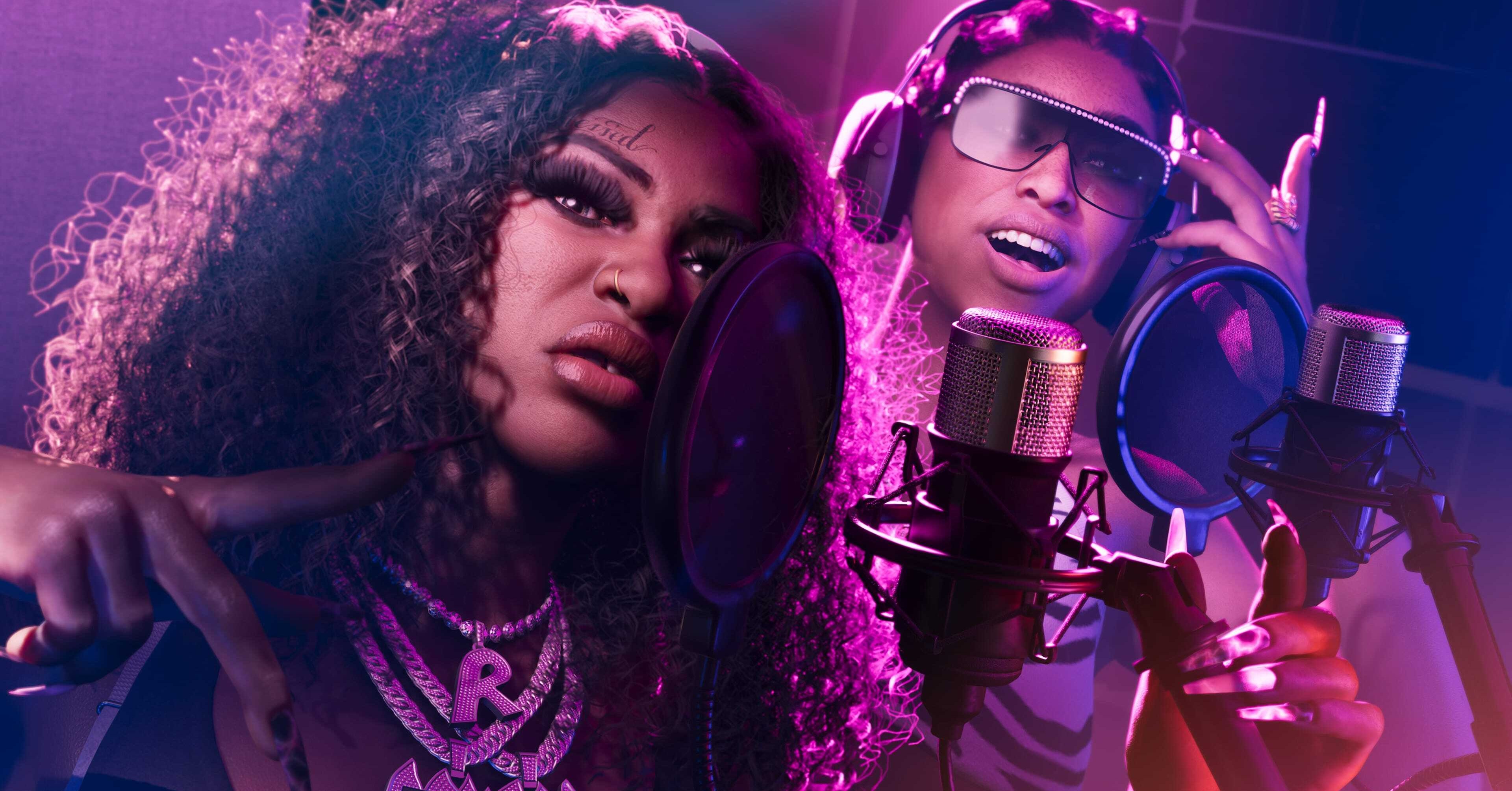 The two female members of Real Dimez, an R&B group in GTA 6, singing into two microphones in a recording studio together