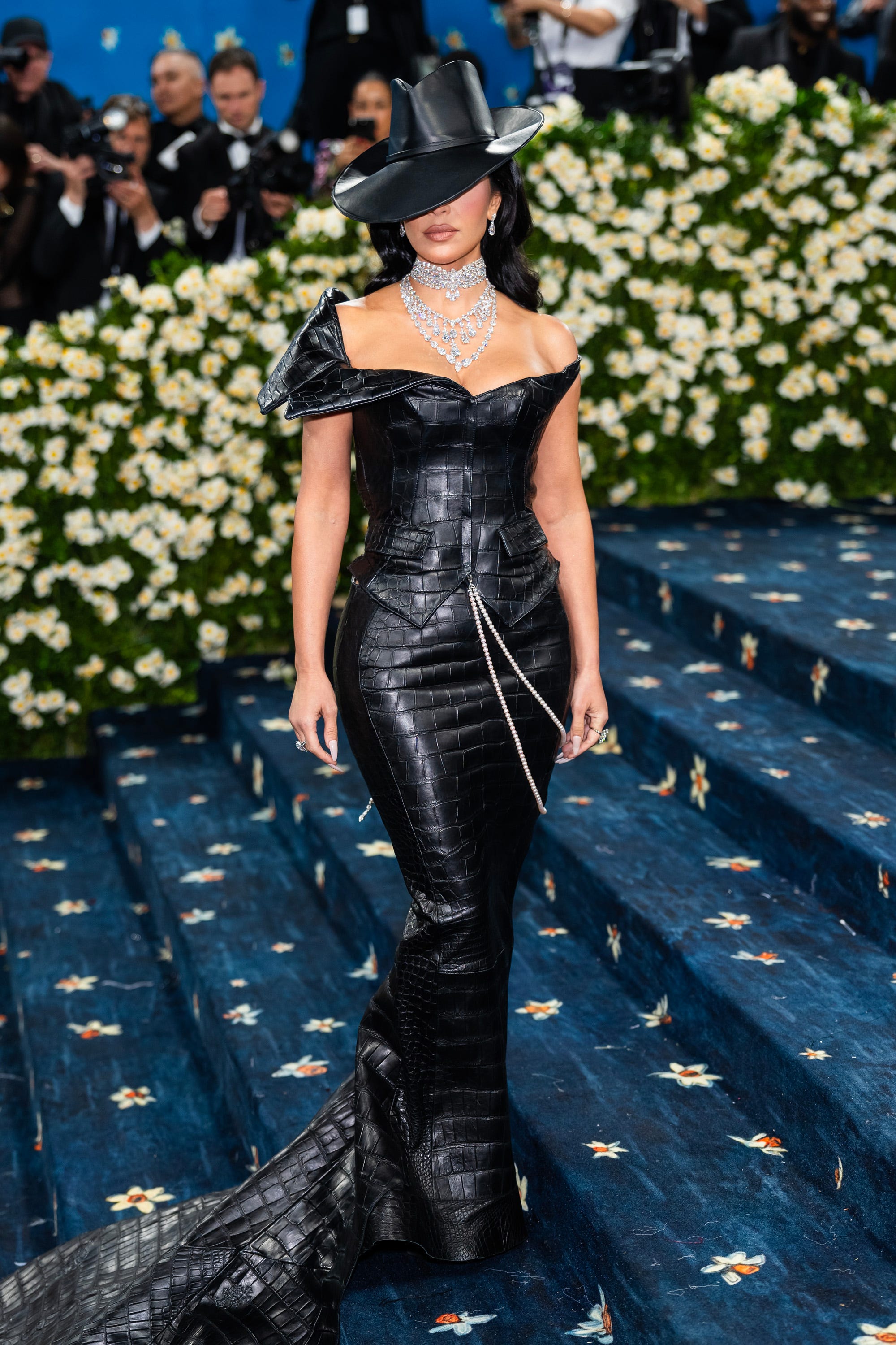 Kim Kardashian poses at the Met Gala in a leather dress and a hat that covers her eyes.