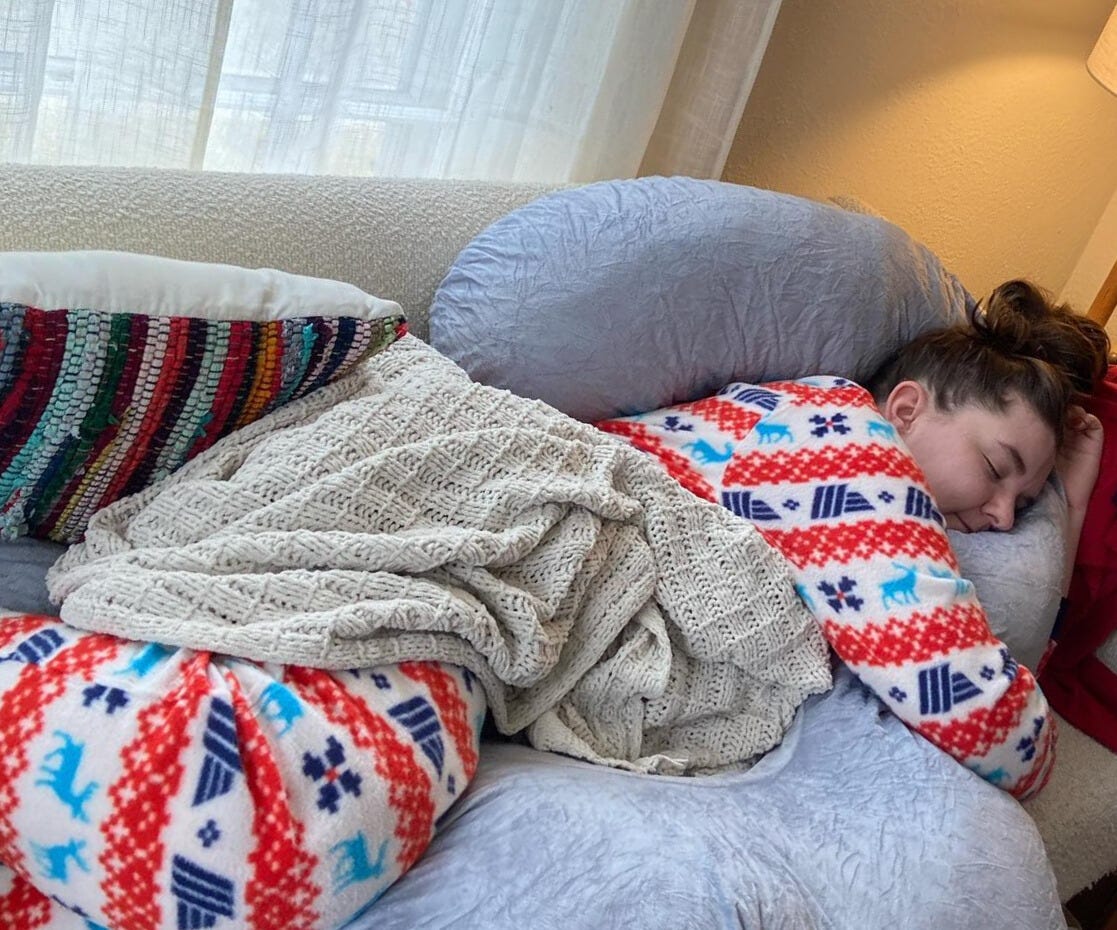 The author taking a nap on the couch with a pregnancy pillow.