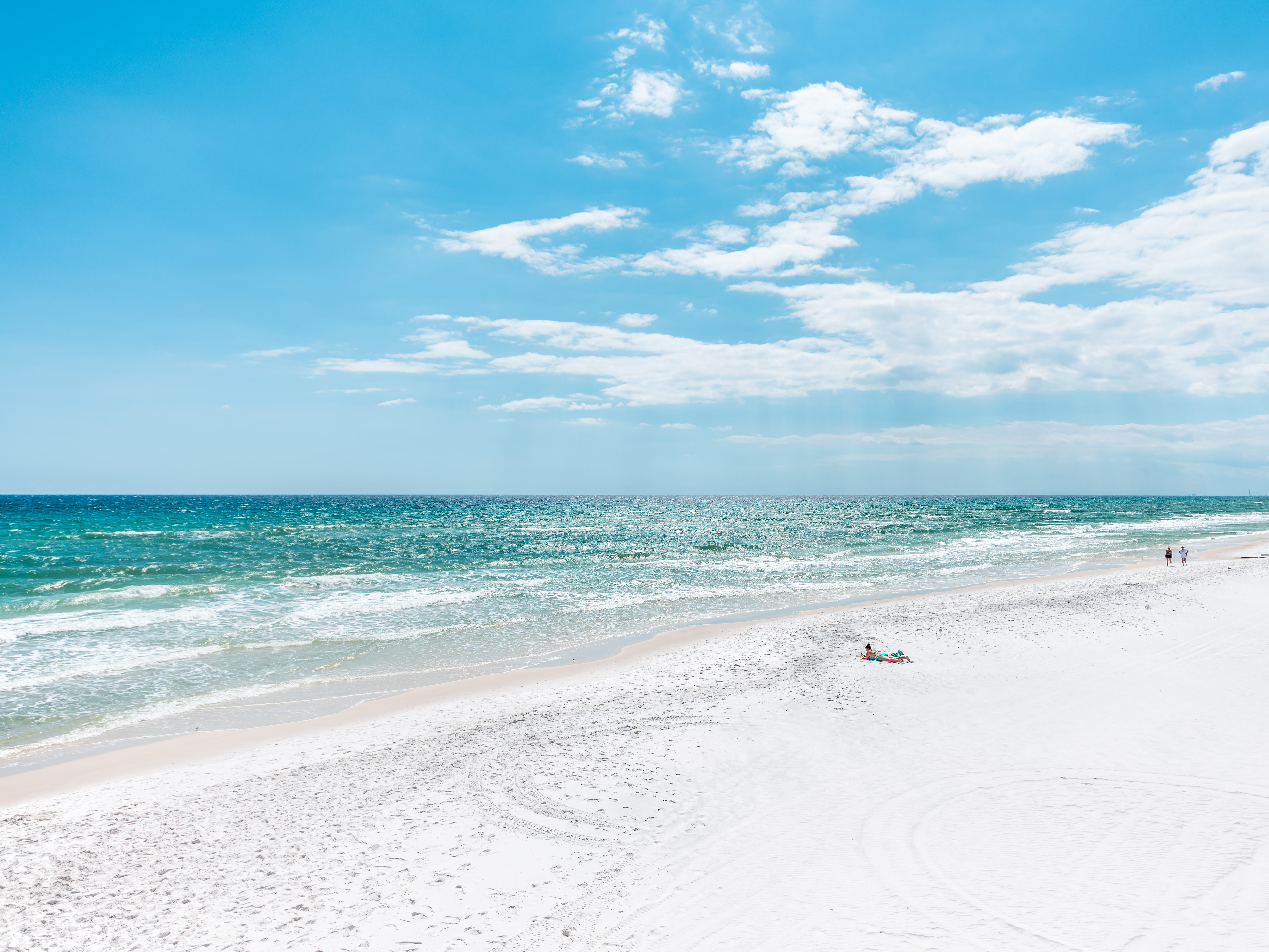 A few people walking or lying on a white-sand beach with turquoise water.