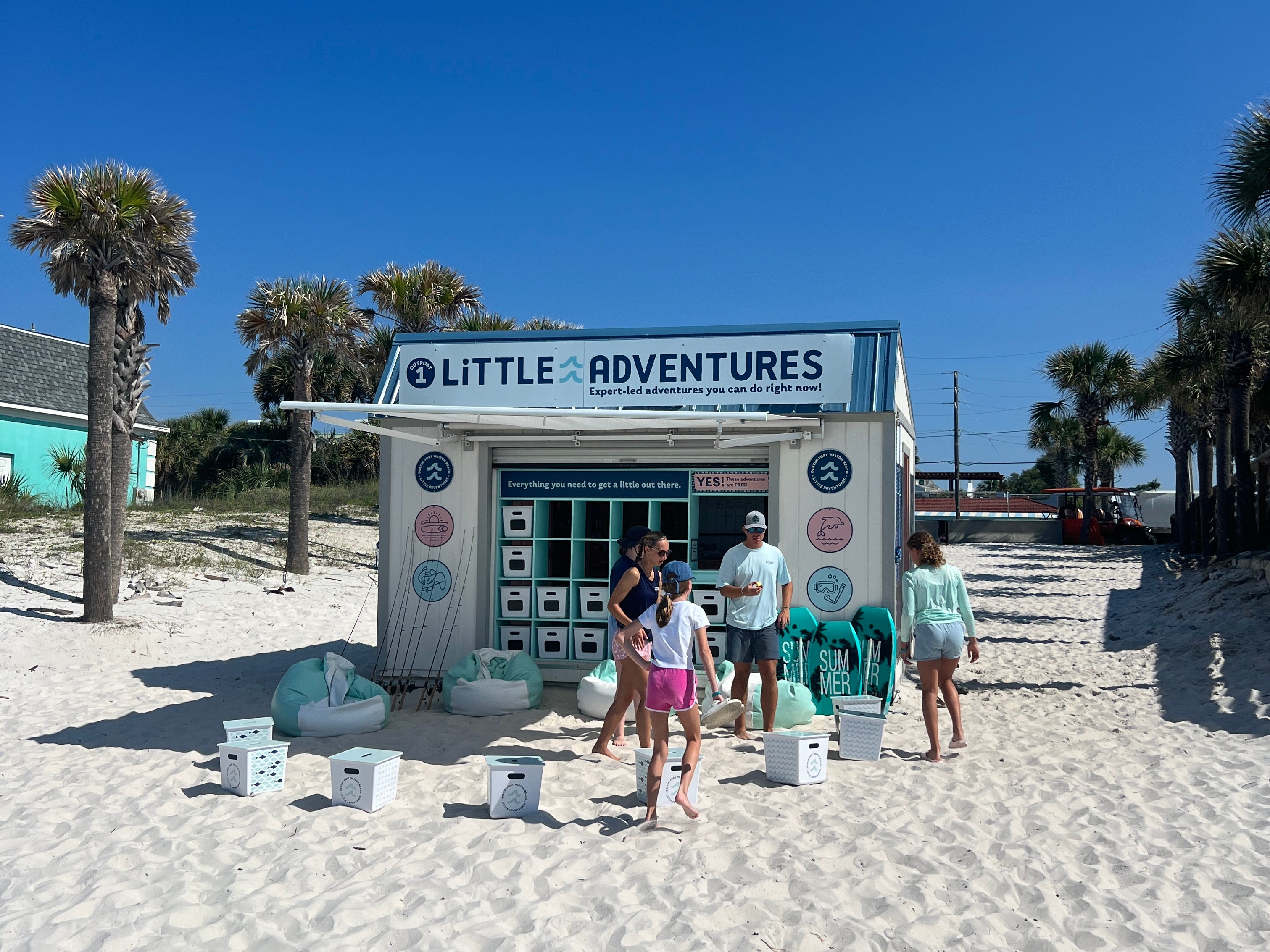 A family of four stand outside a beach shack with a sign that reads, "Little Adventures: Expert-led adventures you can do right now."
