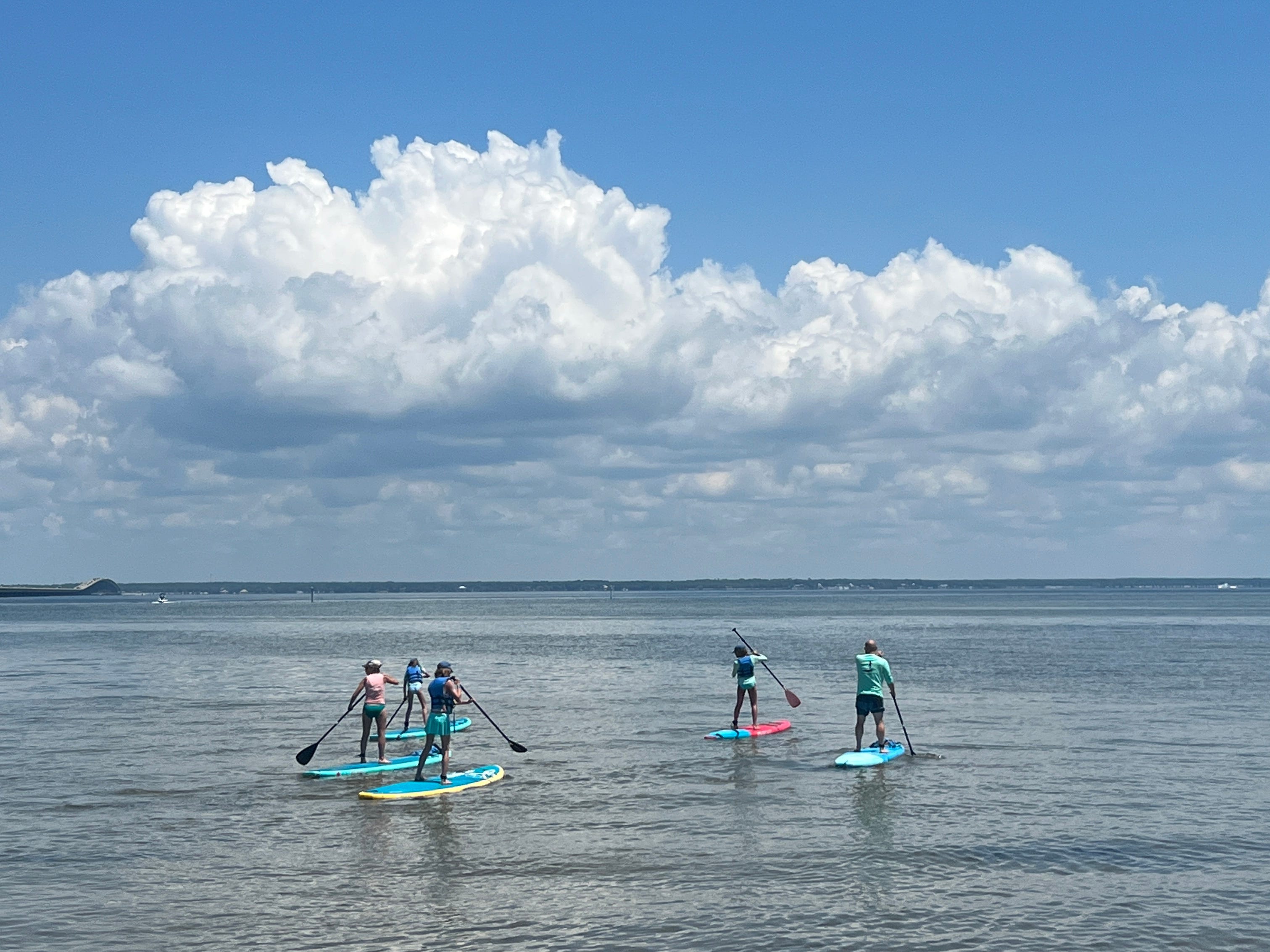 Five people paddleboarding on a partly cloudy day.