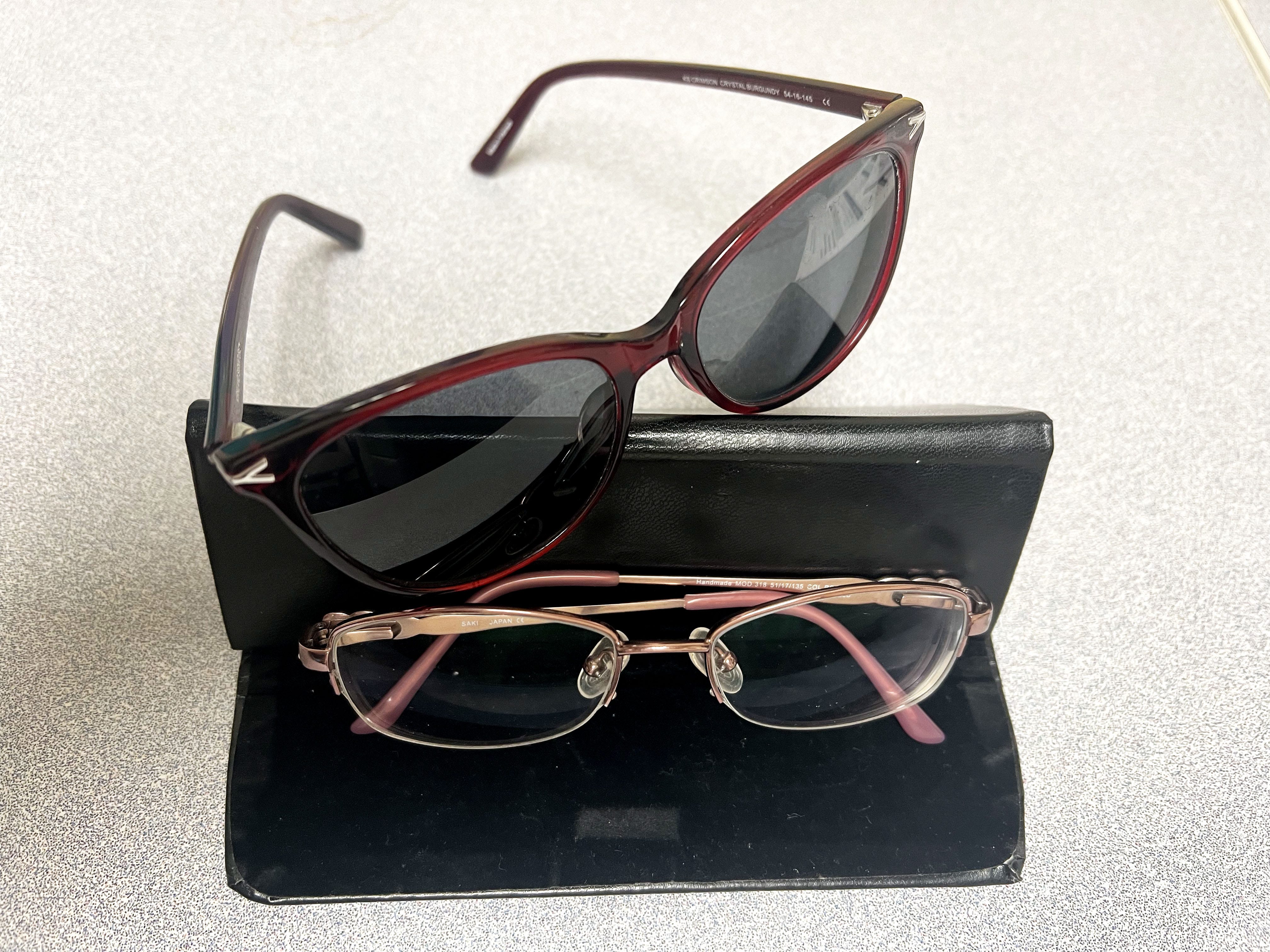A pair of red sunglasses and a pair of eyeglasses photographed with a black case on a white surface.
