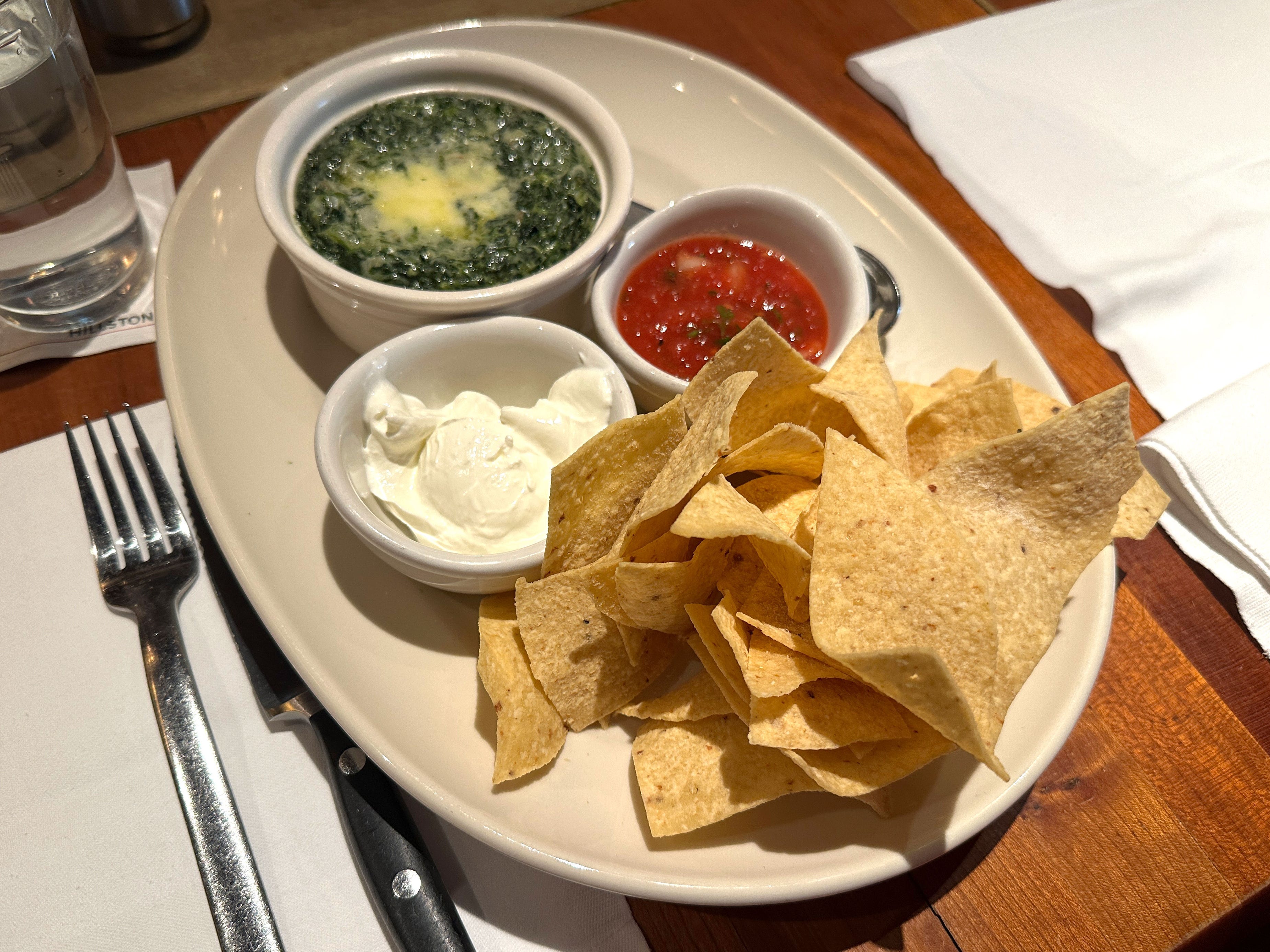 A plate with tortilla chips, artichoke dip, sour cream, and salsa.