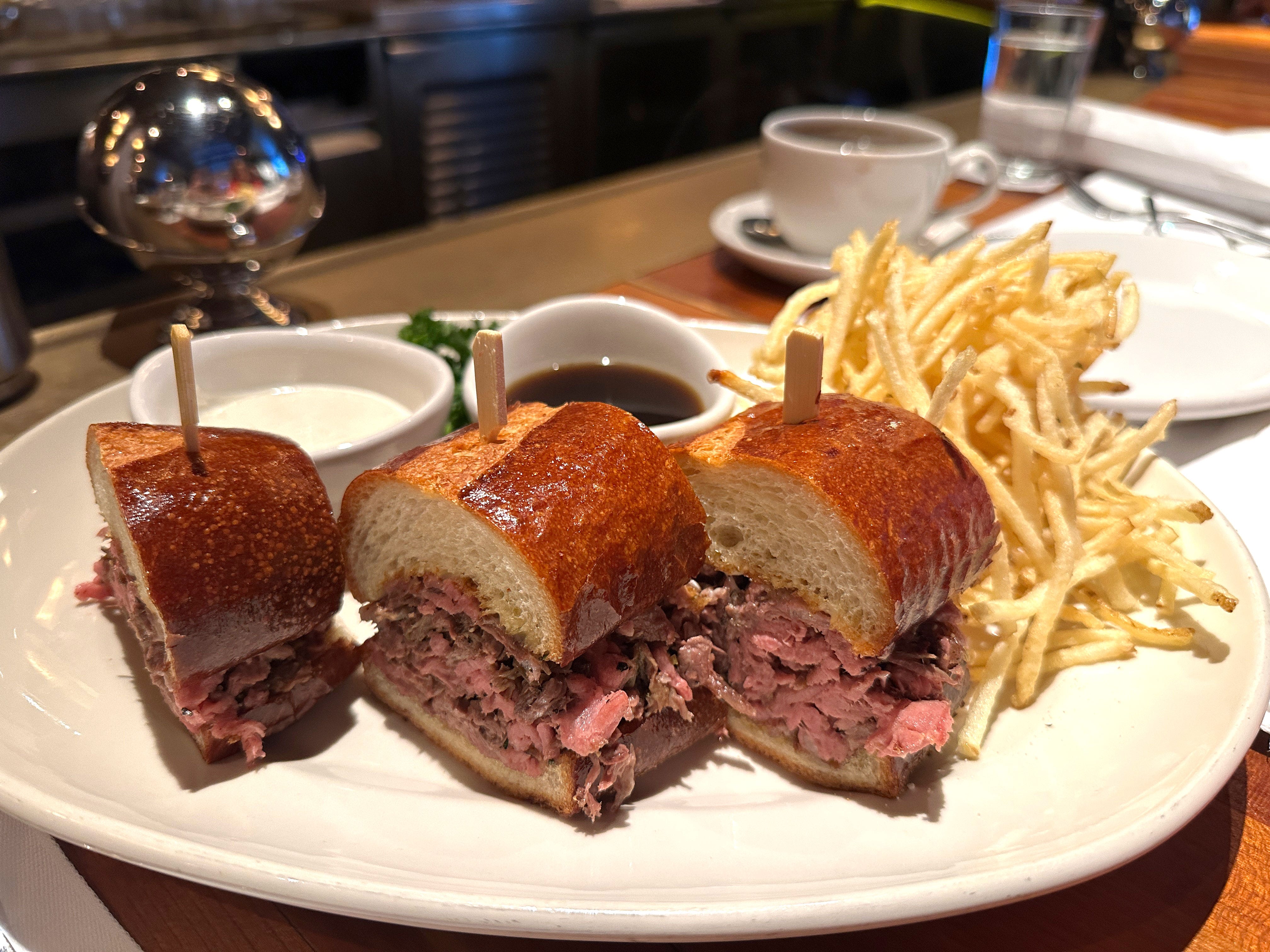Three pieces of a French dip sandwich served with two dipping sauces and fries.