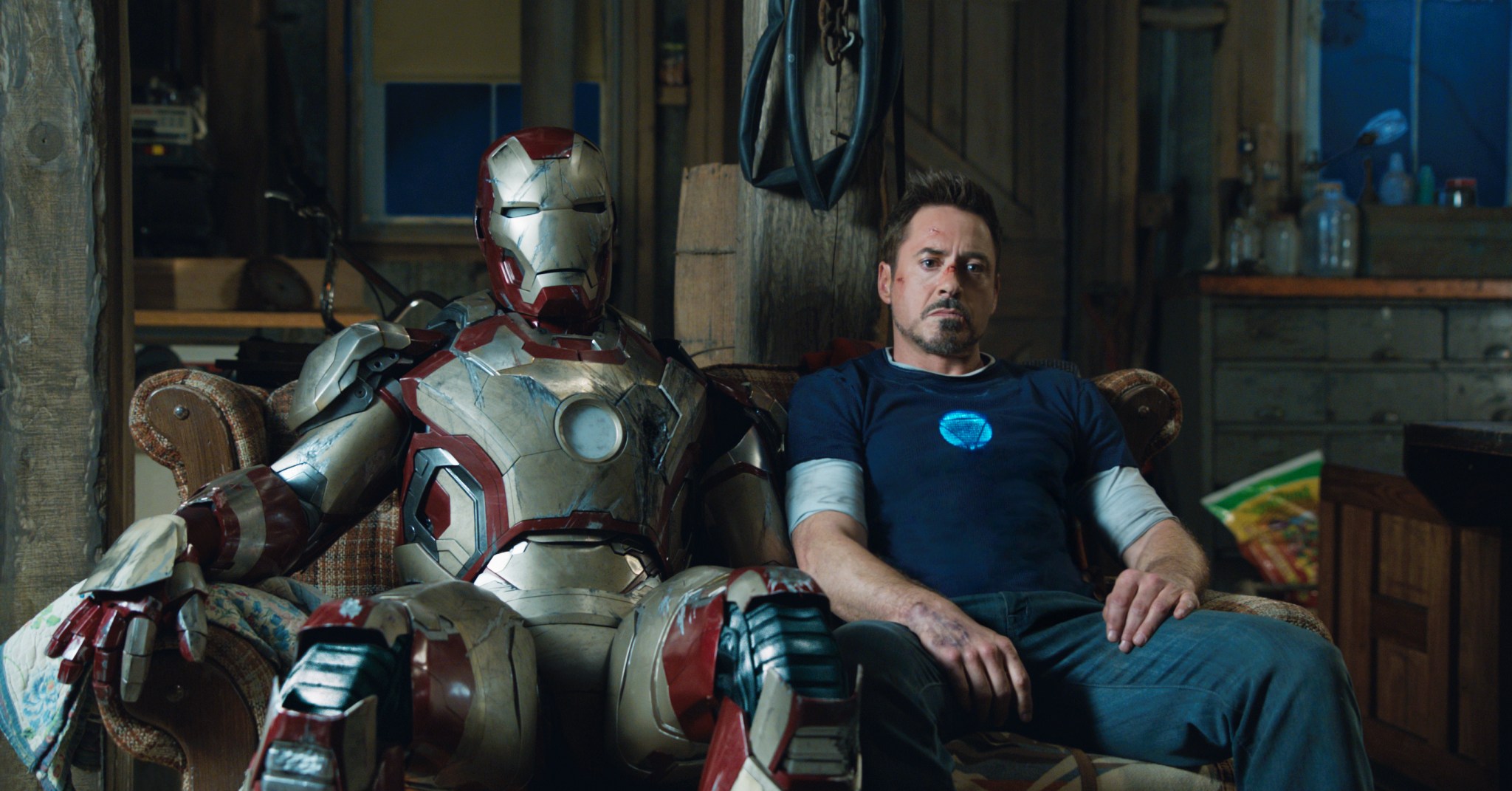 Robert Downey Jr. lounges on a couch next to an Iron Man suit in Iron Man 3.