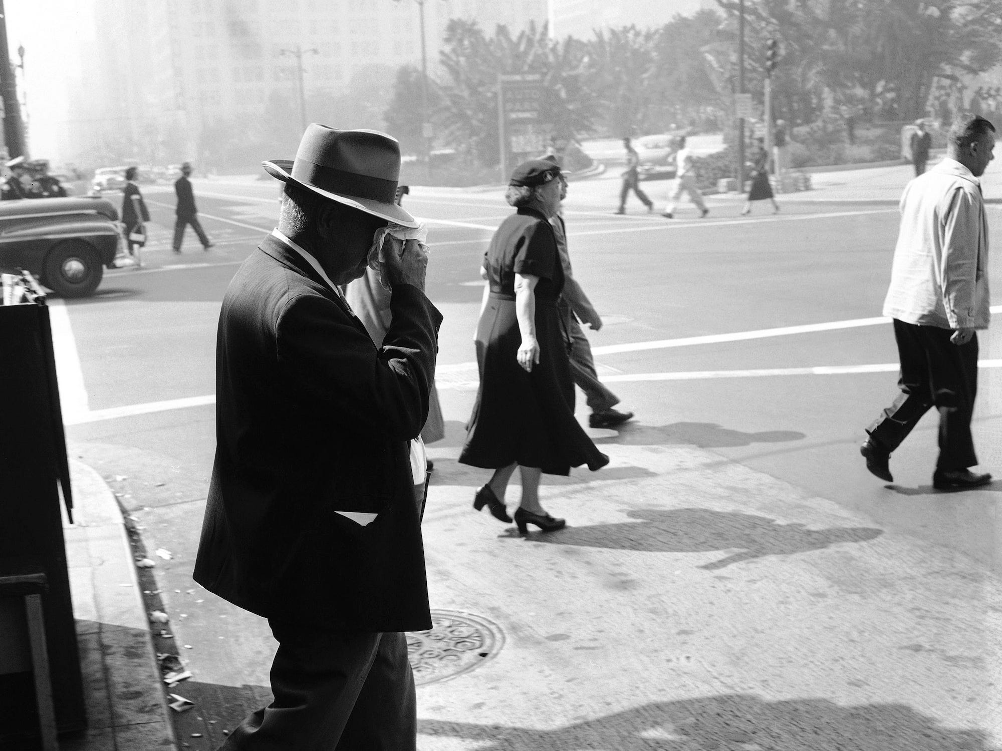A pedestrian wipes his eyes as he crosses a downtown, Los Angeles street, Oct. 15, 1954, the ninth successive day on which an eye-stinging smog blanket has hung over southern California. There were so many red eyes in town, one observer commented that you couldn’t tell the people with hangovers from those who went to bed the night before.