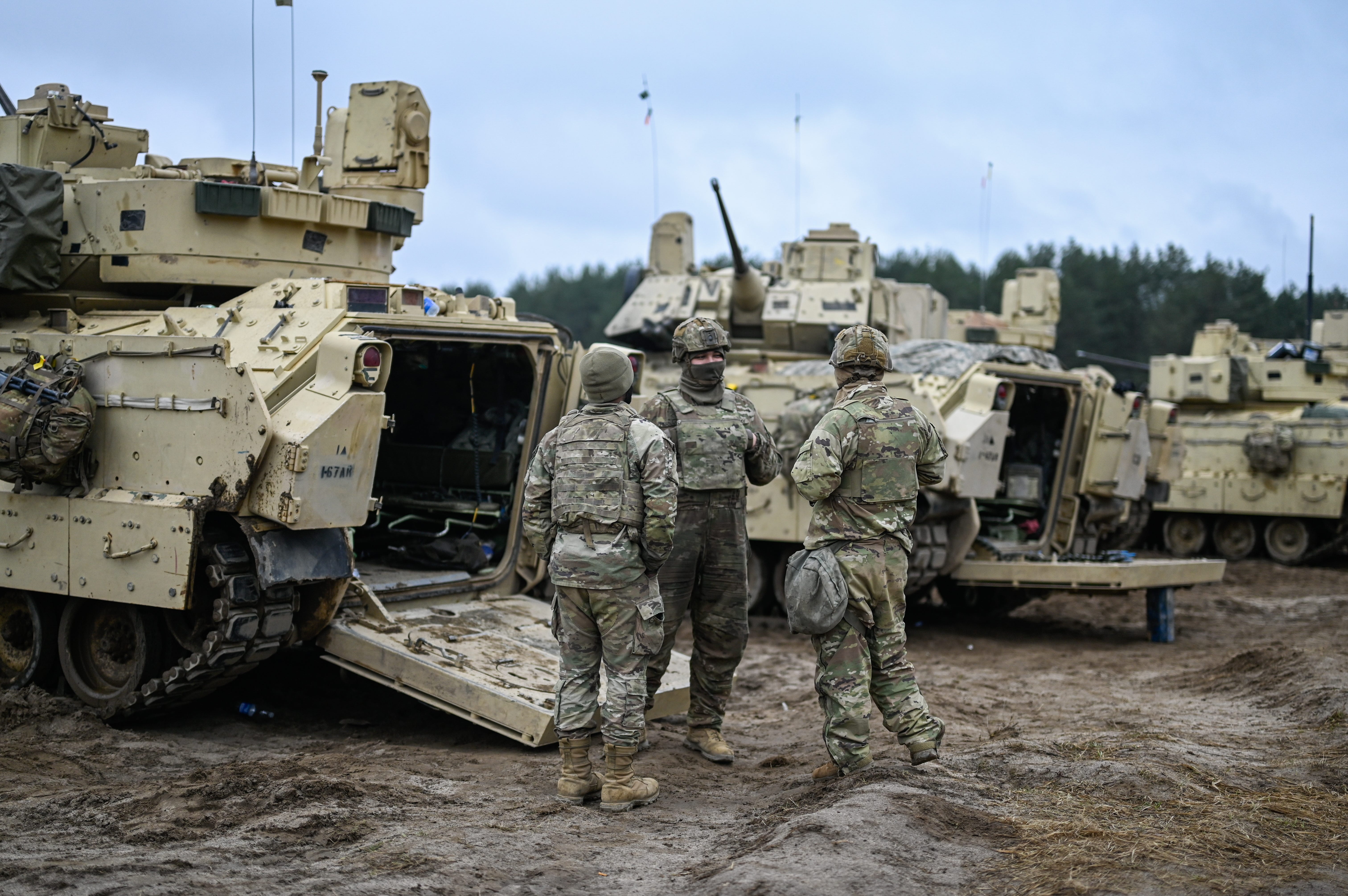 US Army soldiers stand near a line of Bradley fighting vehicles ahead of a live fire exercise.