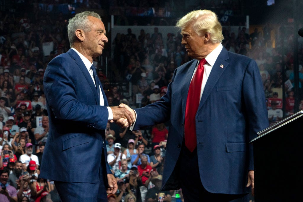 Robert F. Kennedy Jr. shaking hands with Donald Trump with a crowd of supporters behind them.