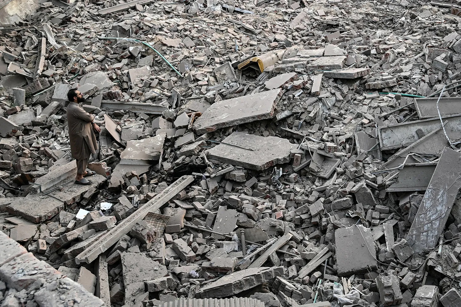 A man stands atop a wide field of concrete debris from a destroyed building.