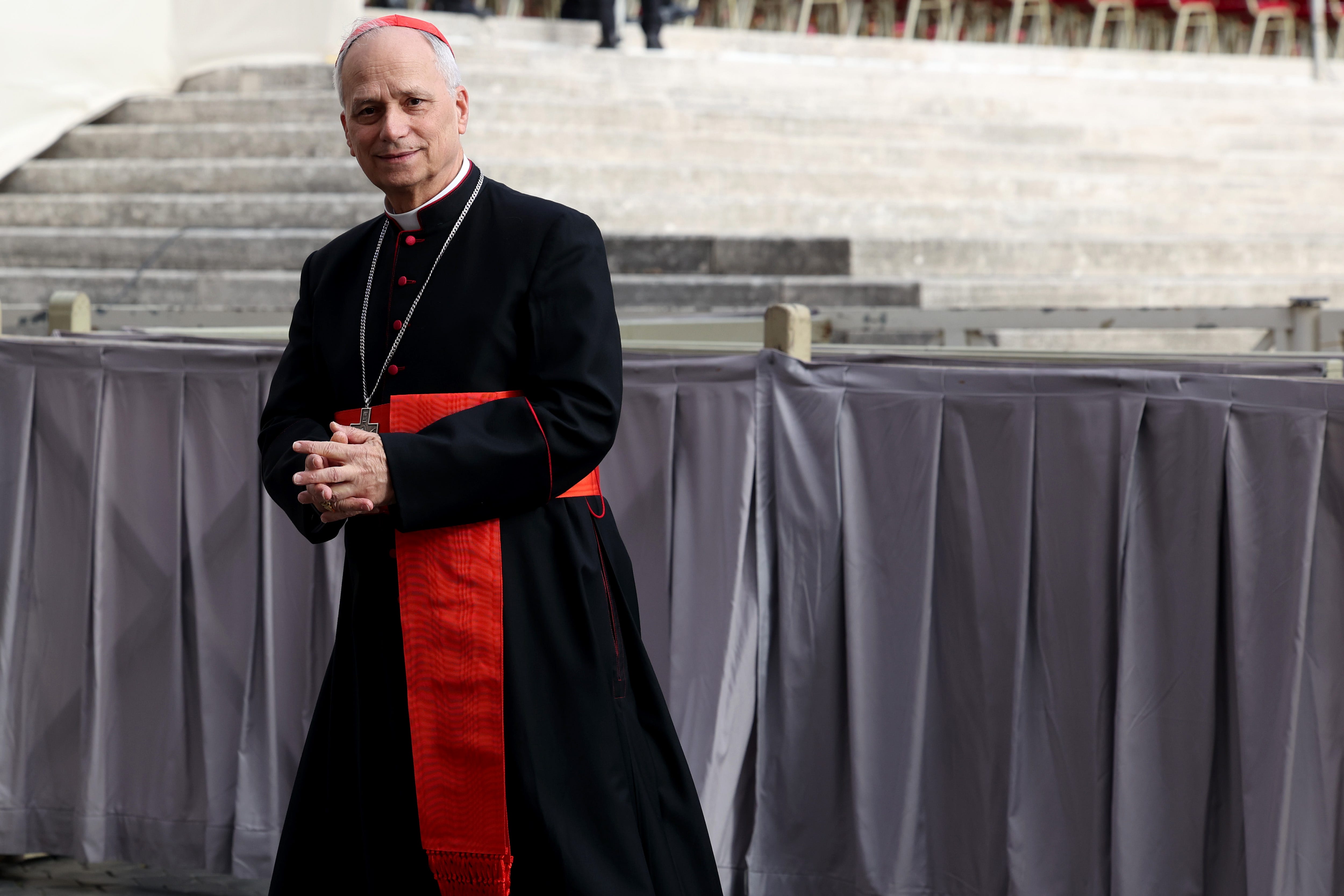 Pope Leo XIV wearing black and red clasping his hands together