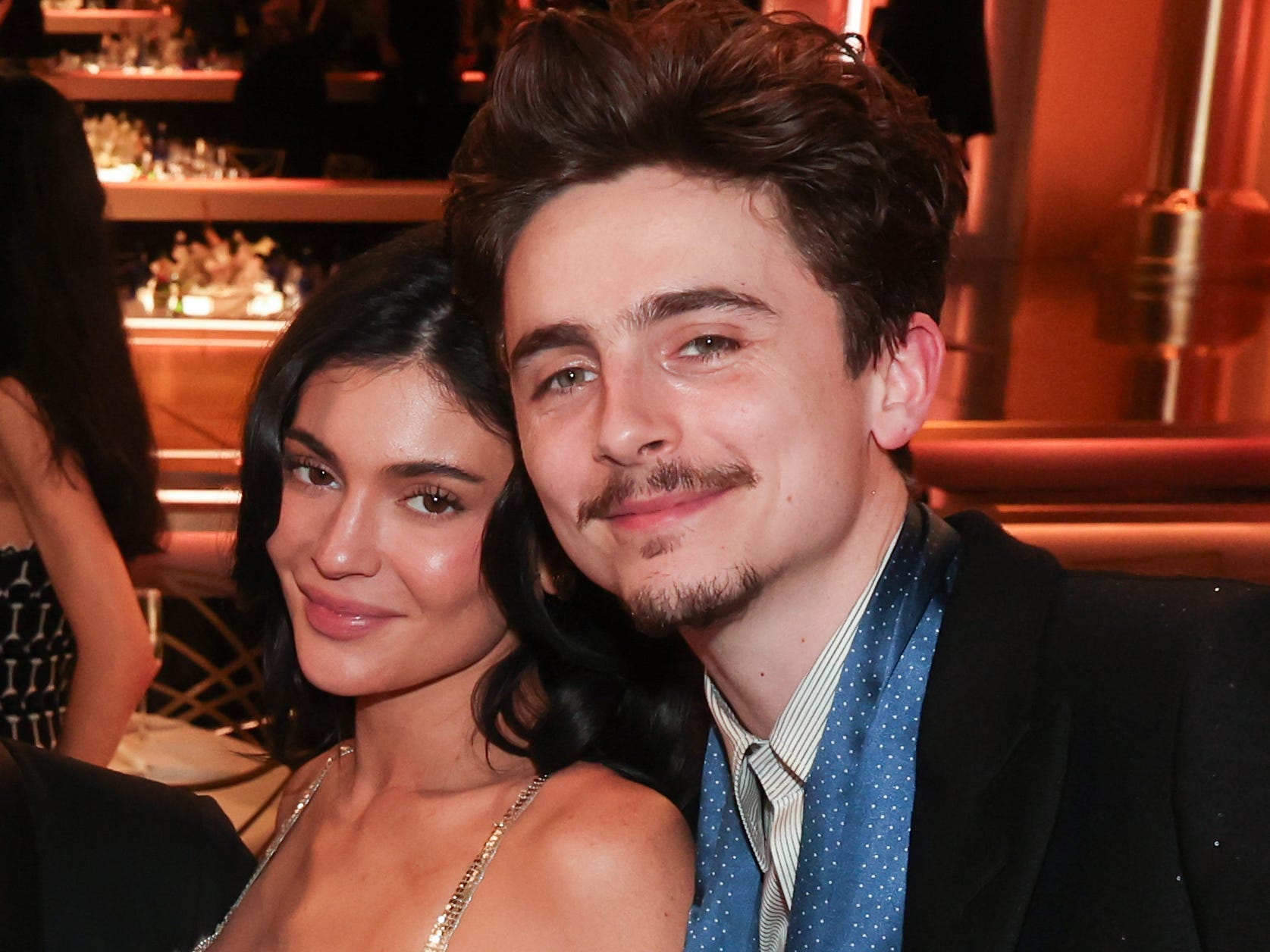 kylie jenner and timotheee chalamet together at the golden globes. kylie is wearing a low cut silver dress nd timothee is standing next to her wearing a black suit with a blue scarf