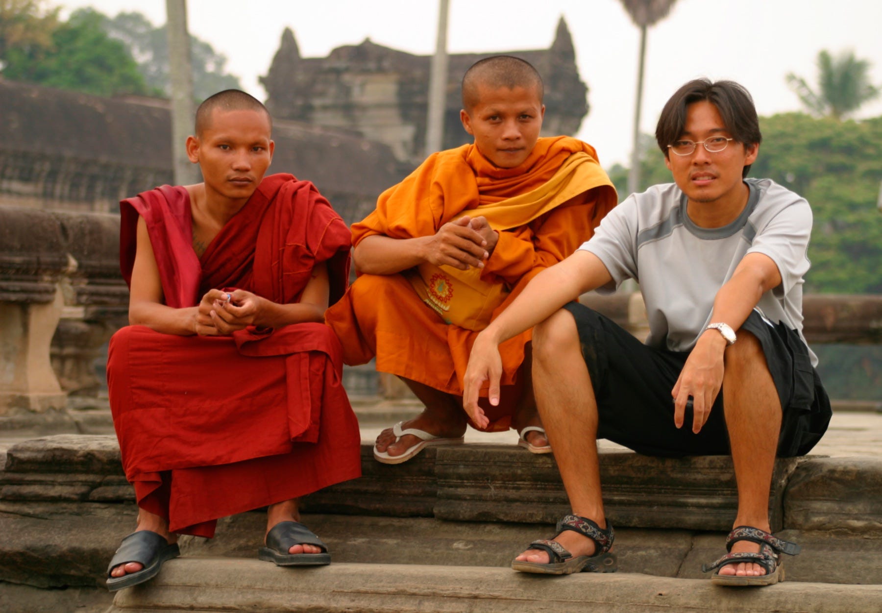 A man sitting on steps with two monks dressed in orange robes.