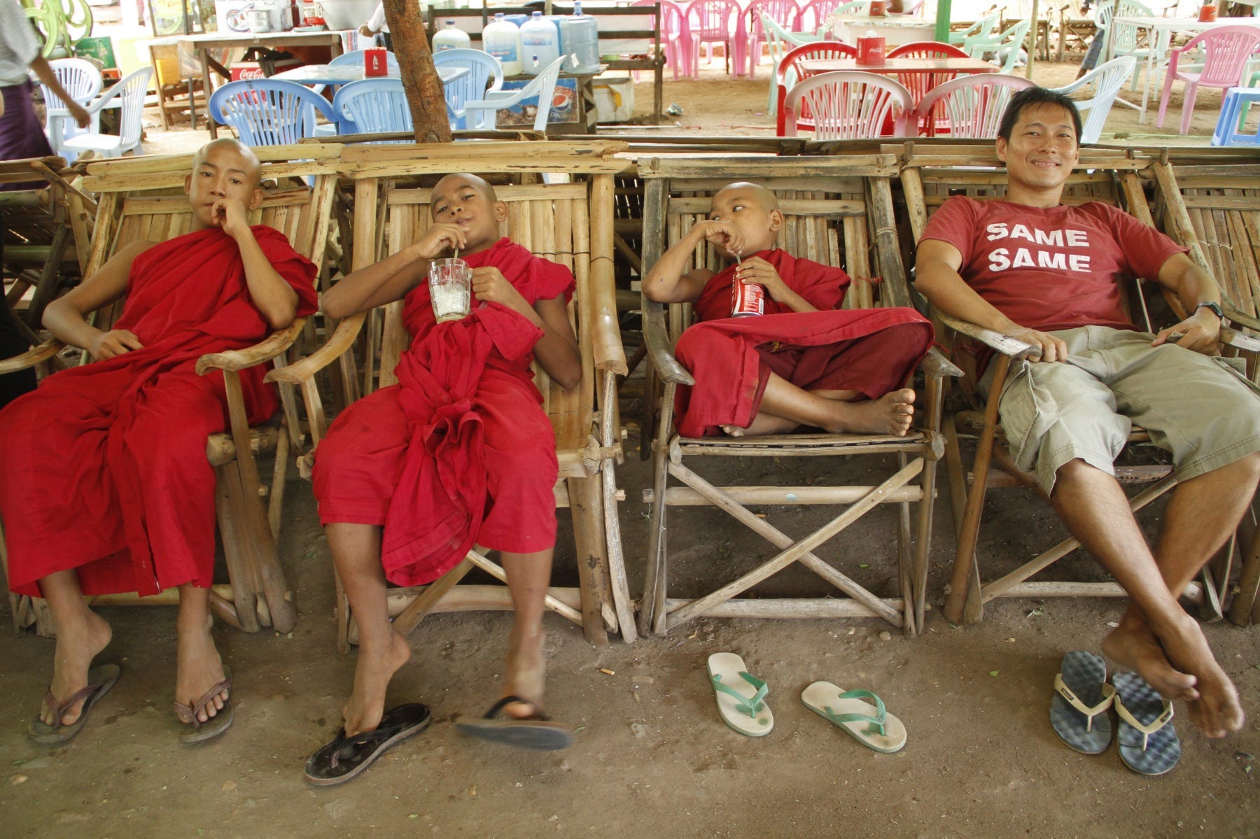 A man wearing a red shirt that says "Same Same" sitting next to three monks in red robes.