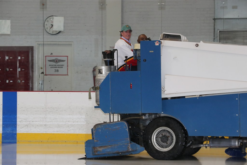Doug Burgum driving the Zamboni with Zamboni operator Reginald Devilme