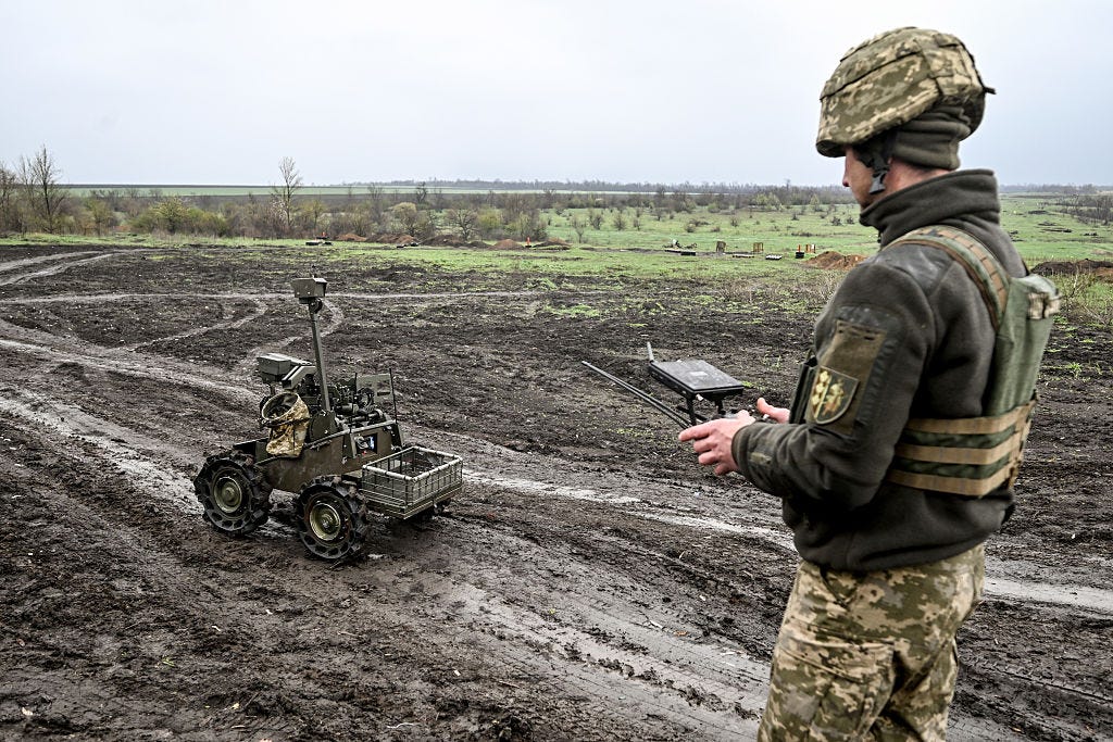 A Ukrainian soldier stands in the mud and remotely controls an uncrewed ground vehicle.