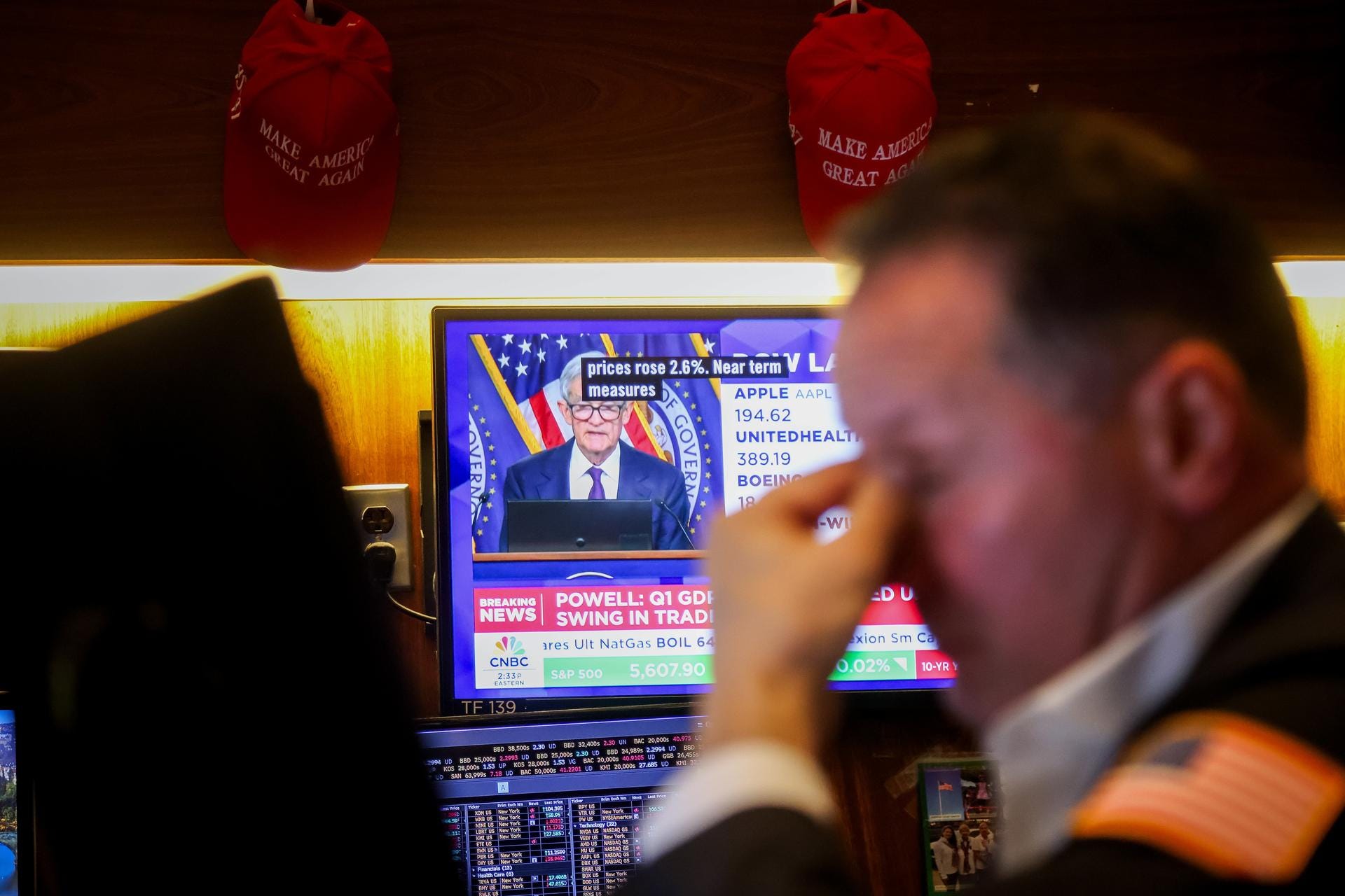 A trader with his hand on his brow, and Fed chair Jerome Powell on CNBC TV in the background.