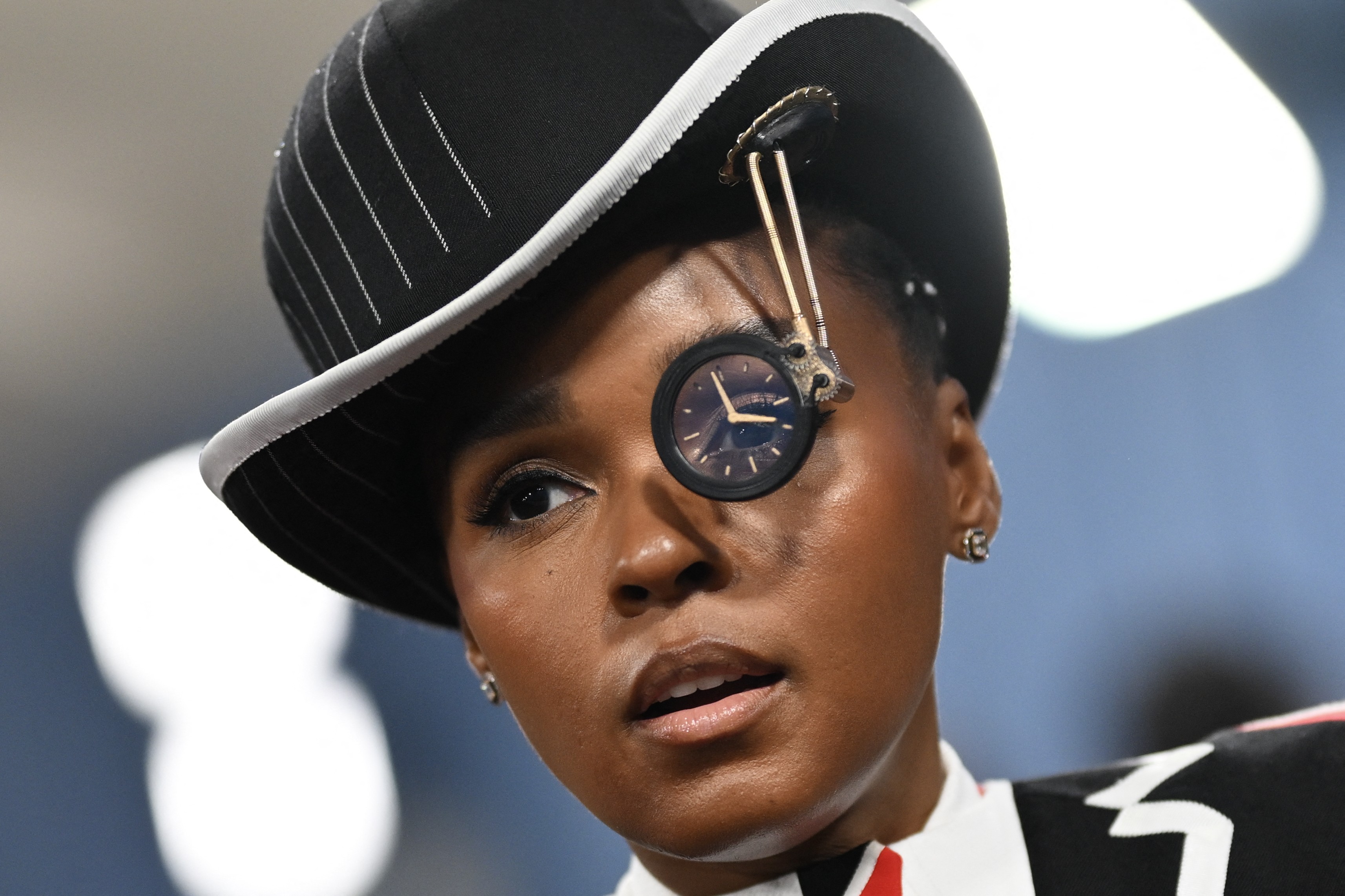 Janelle Monae wears a costume, including a hat with an unusual eyepiece attached to its brim.