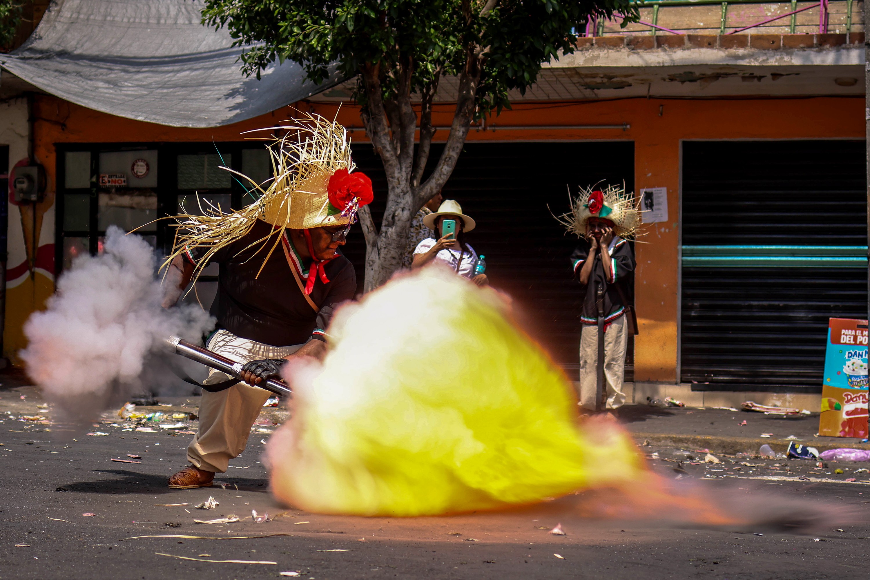 A person wearing a costume detonates a gunpowder charge in a street during a festival.