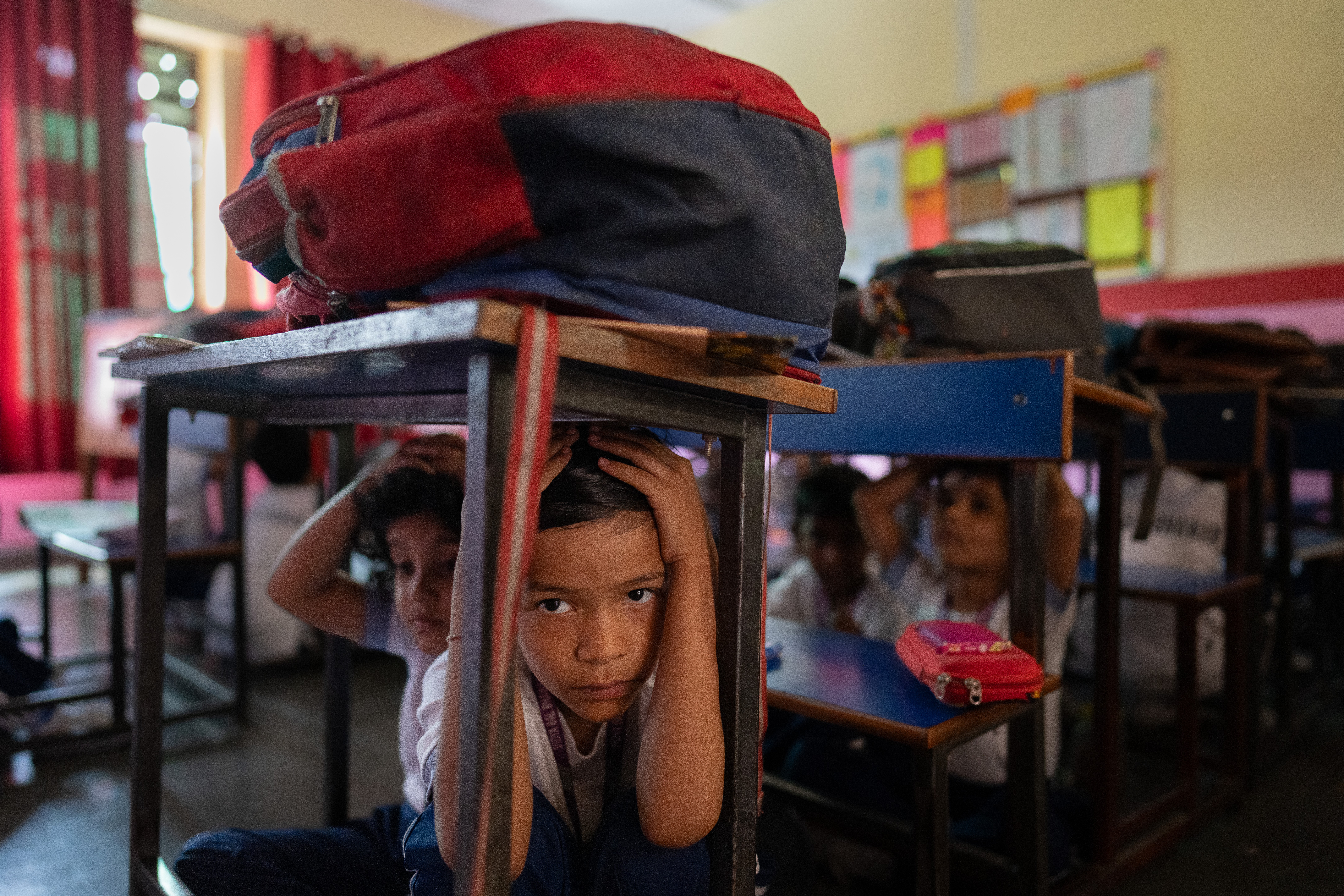 Several young students crouch down beneath their desks in a classroom during a drill.