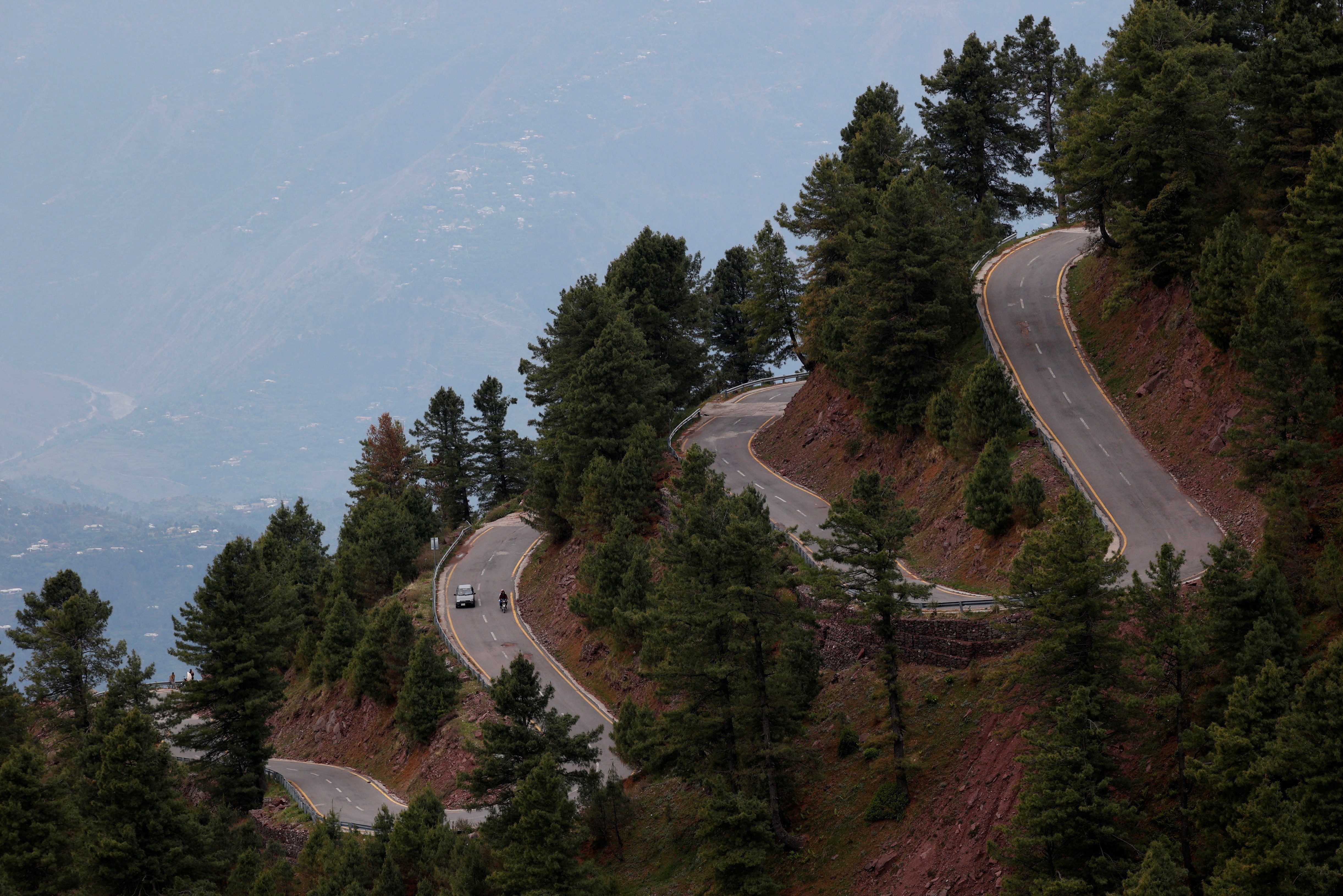 Several cars navigate a twisty switchback road up a steep hillside.