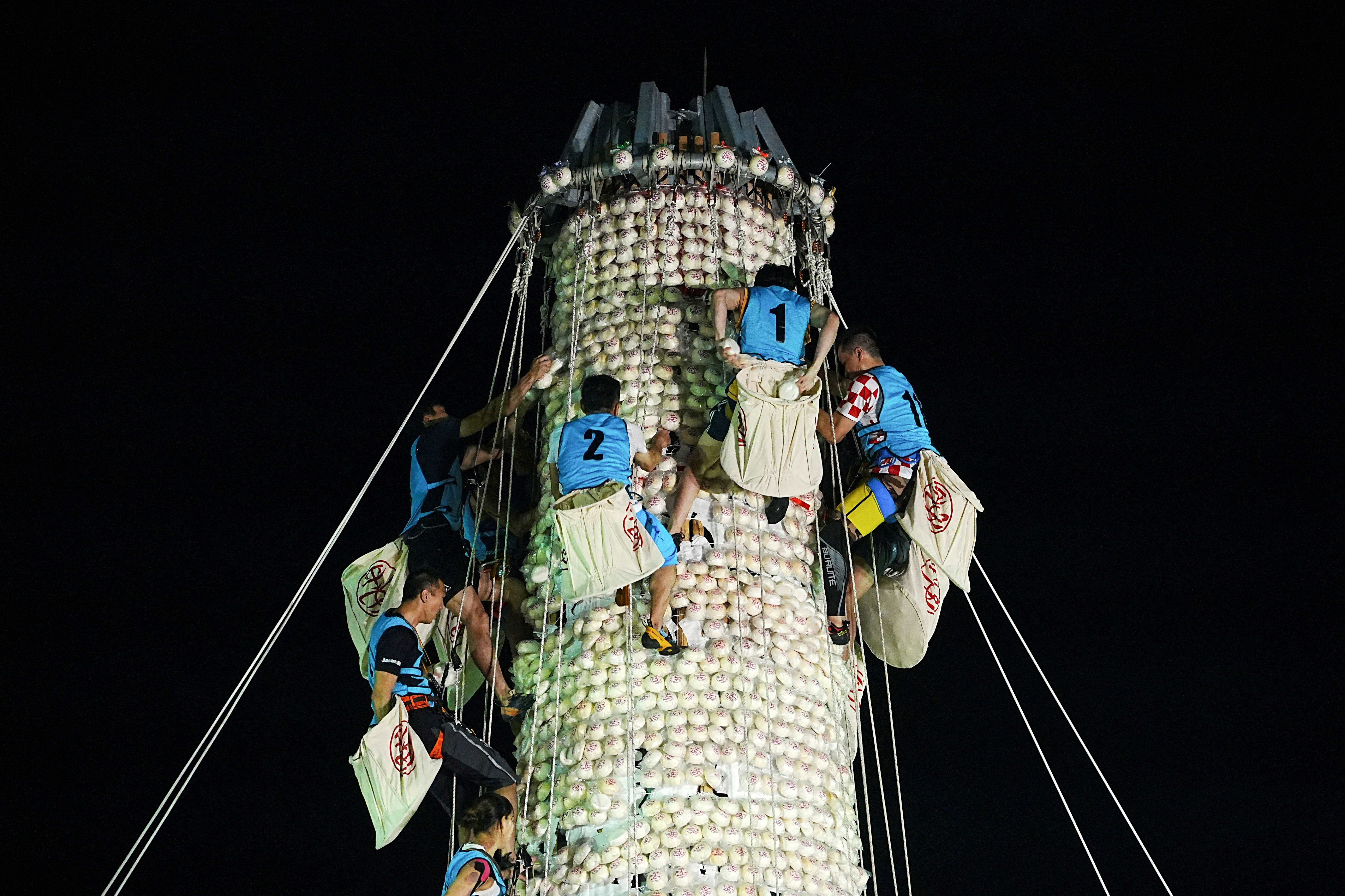 Several competitors climb up a tall pole while gathering buns that have been attached to the pole.