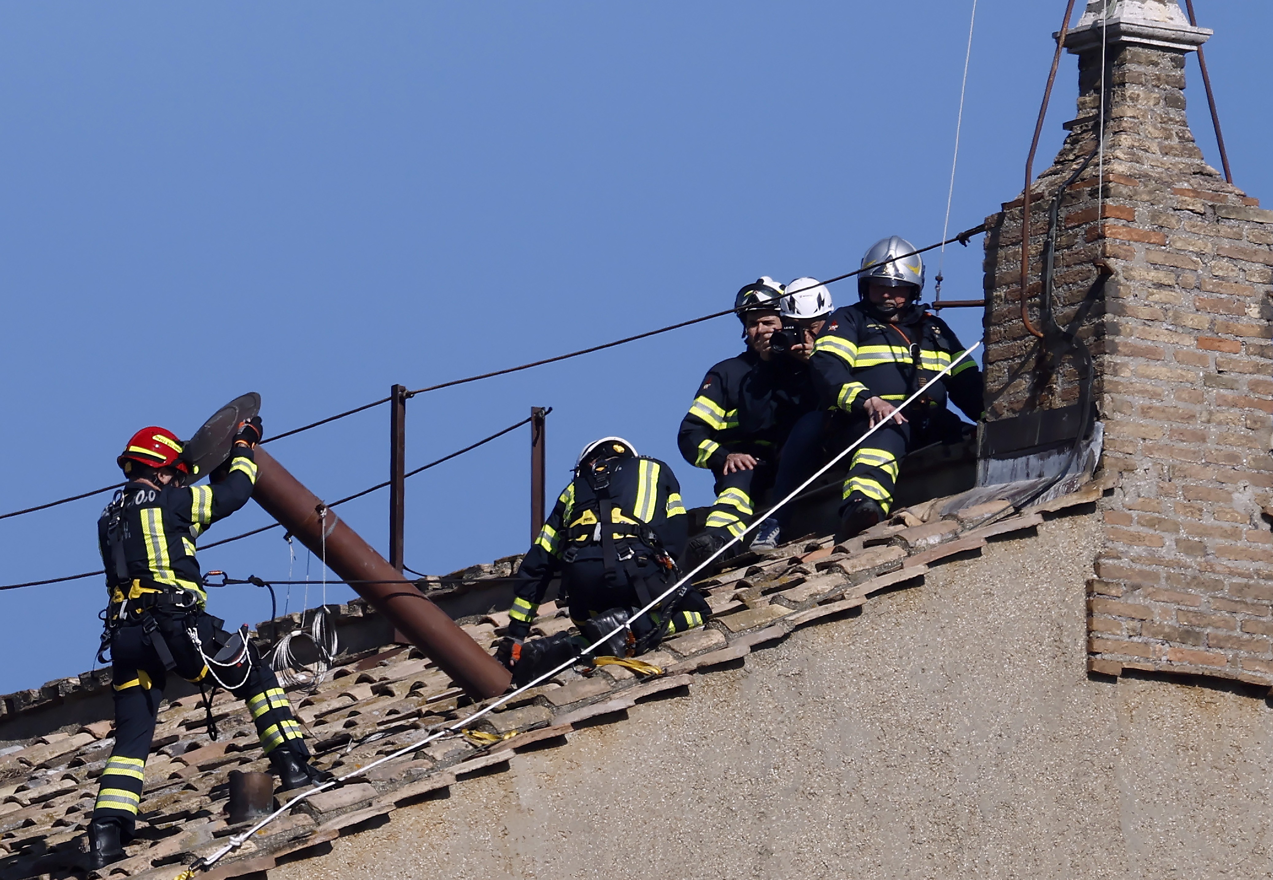 Several firefighters install a temporary chimney on a roof.