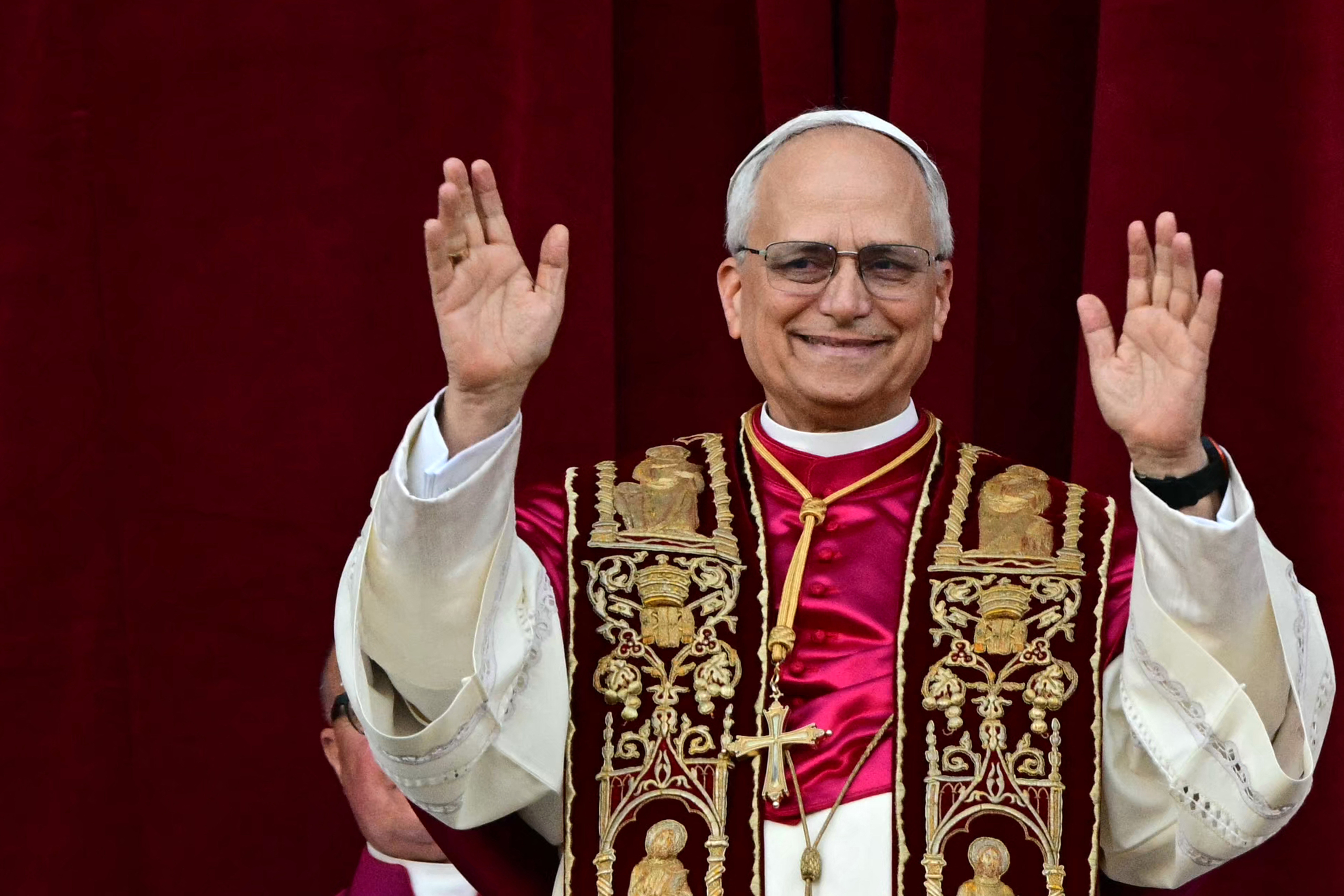 Newly-elected Pope Leo XIV raises his hands, greeting a crowd from a balcony.