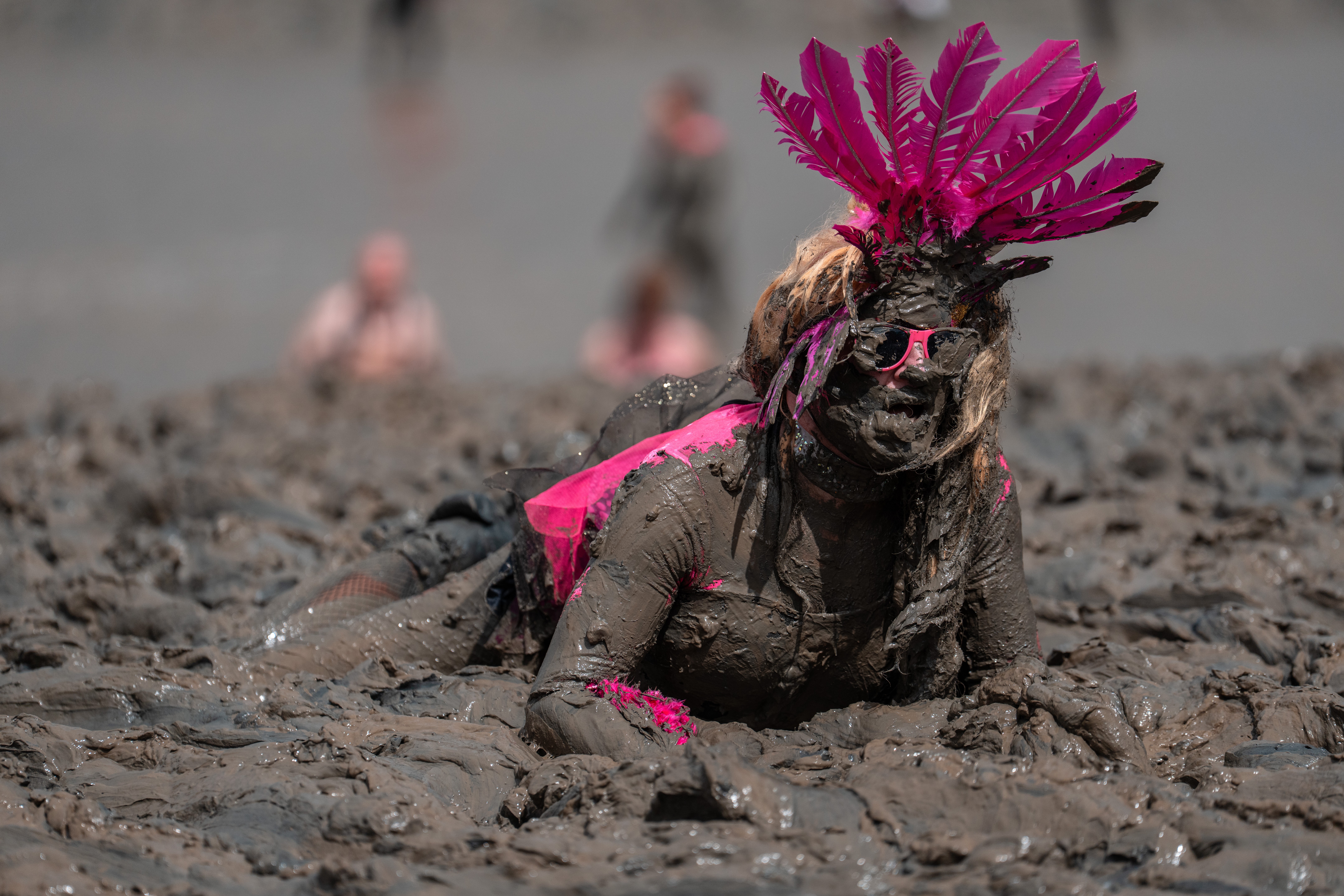 A woman in costume, covered in mud, crawls across a muddy plain.