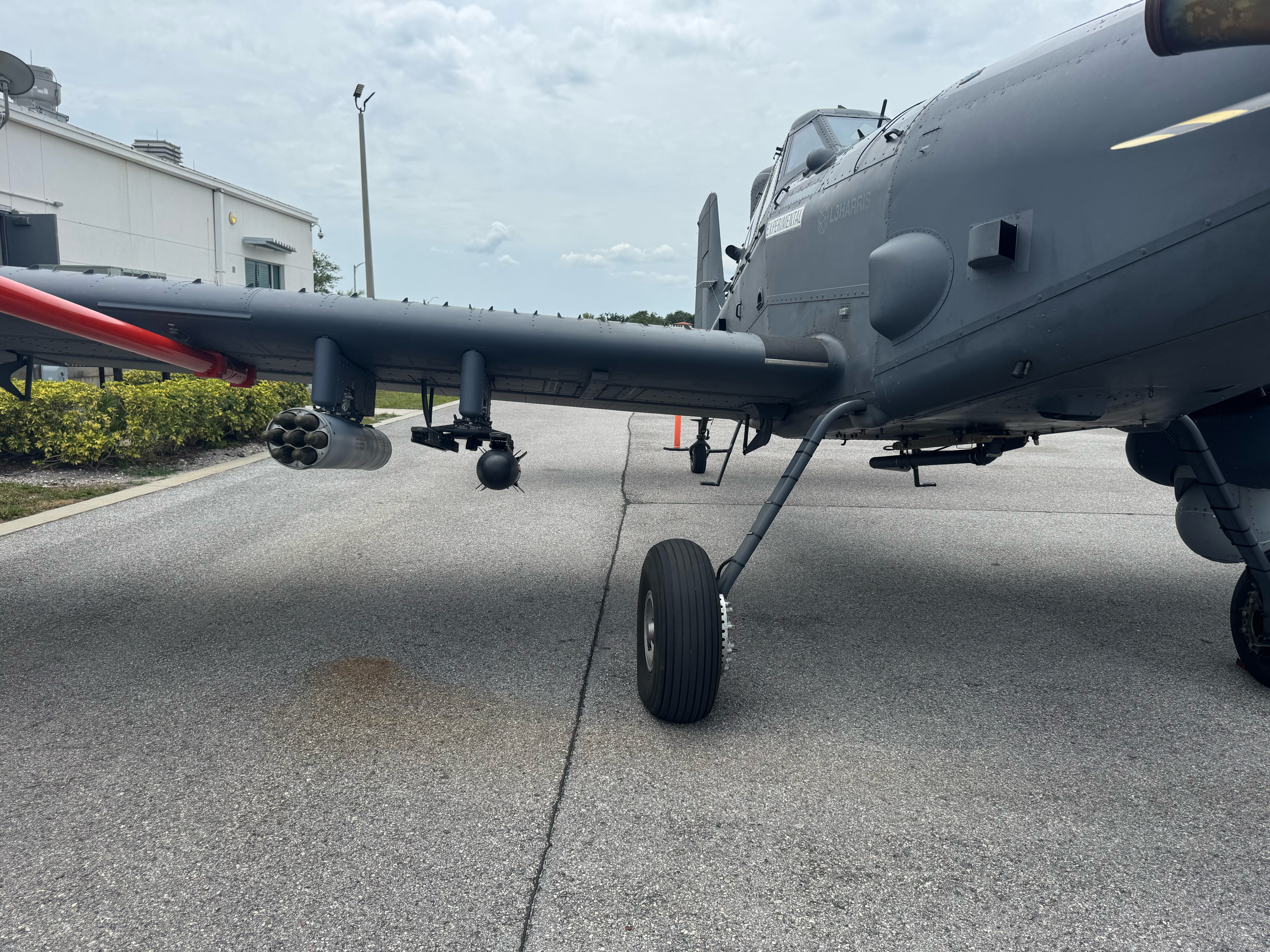 The right wing of L3Harris' Sky Warden plane is seen sitting on an airfield with an overcast sky in the background.