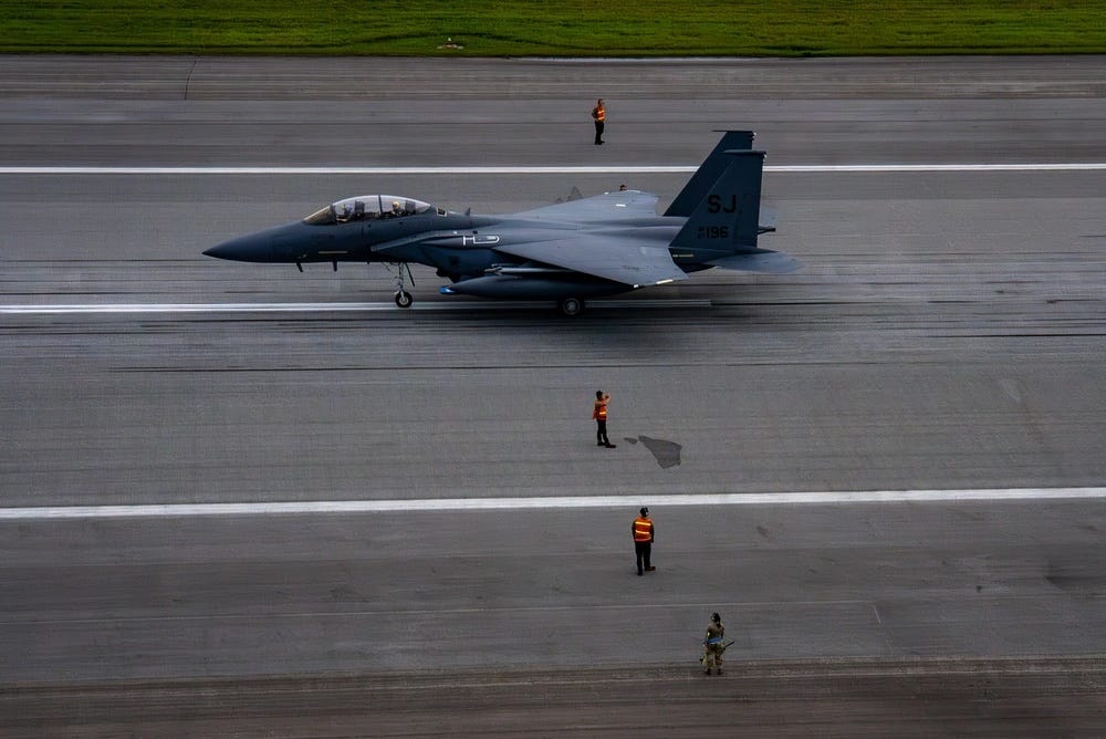 US Air Force airmen marshal aircraft on a runway next to an F-15E Strike Eagle.