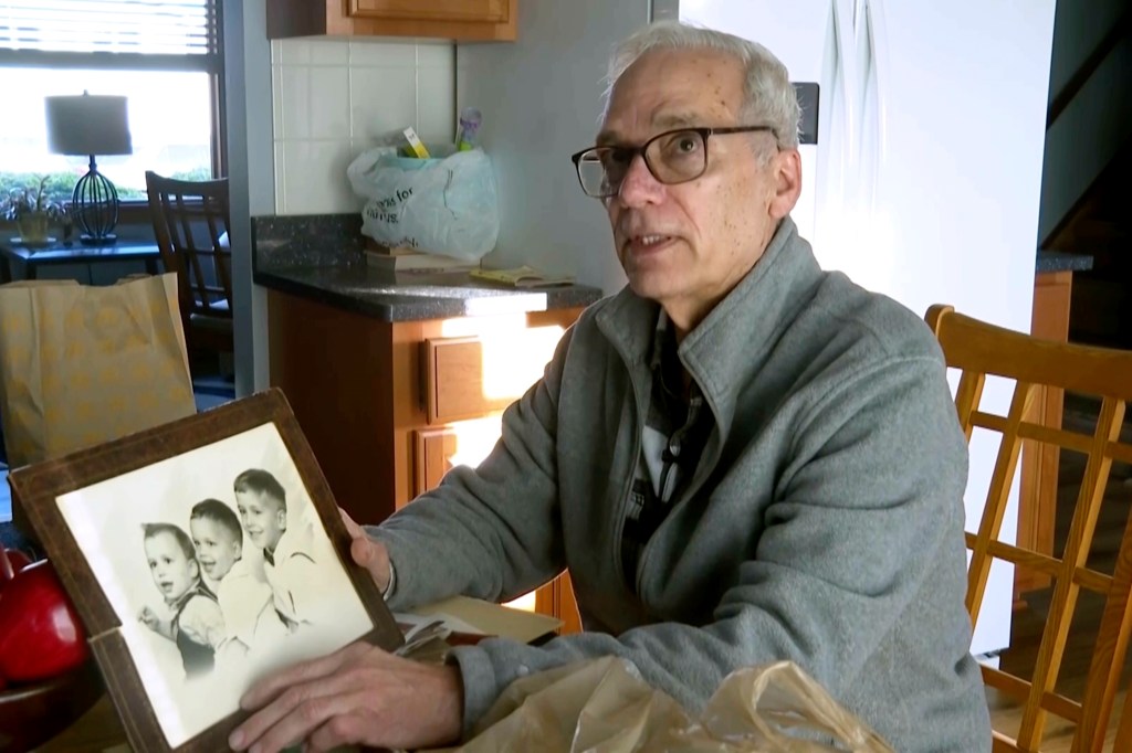 John Prevost holds a family portrait of the three Prevost brothers from 1958.
