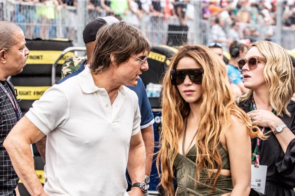 Tom Cruise on a race track next to Shakira who is wearing sunglasses. 