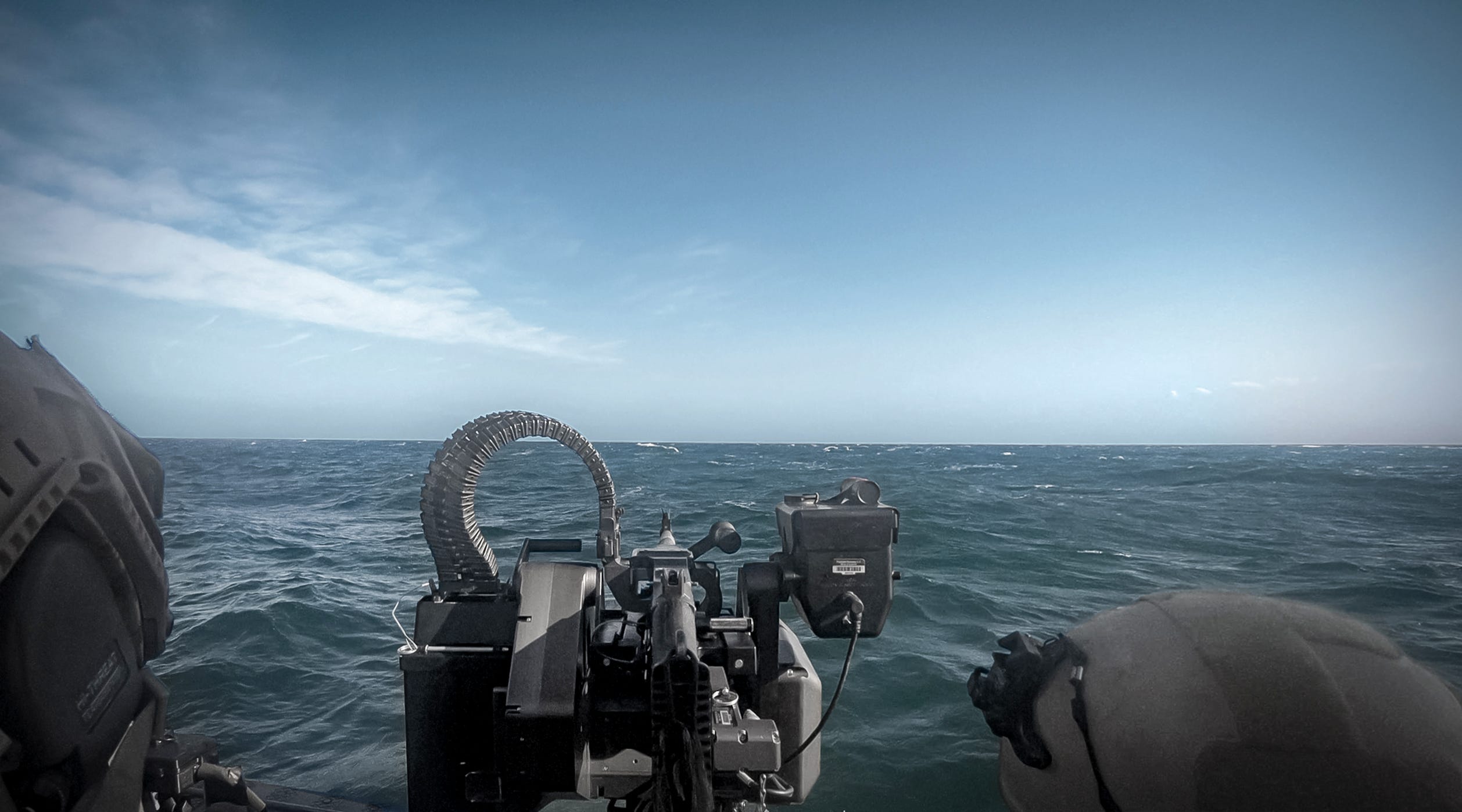 An automated machine gun points out towards the blue ocean with a blue sky in the background.