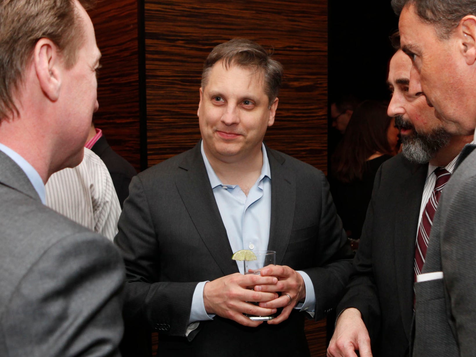 John Overdeck holds a glass while wearing a suit and speaking to several other people