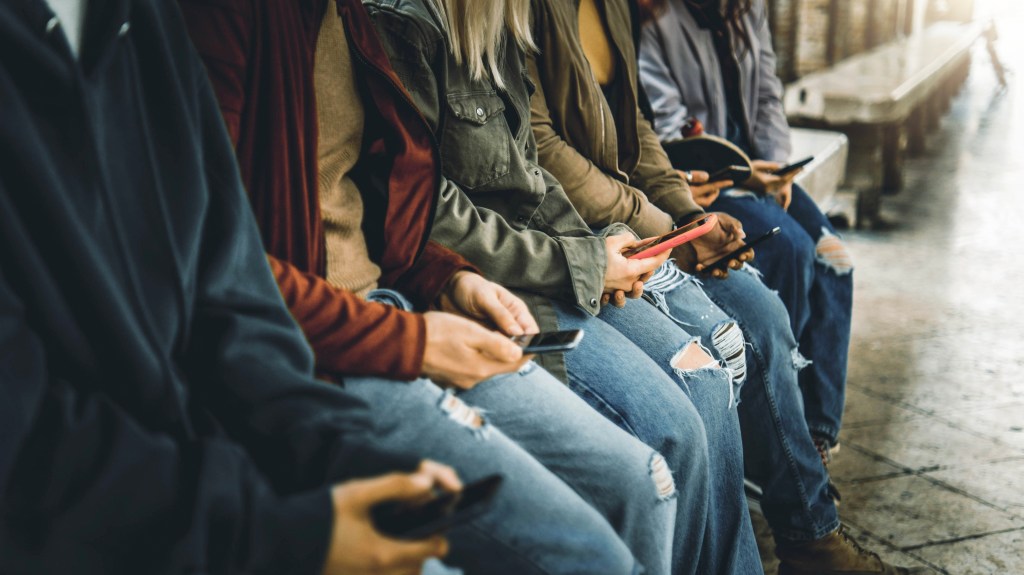 Group of millennial teens using their smartphones outdoors in a social setting