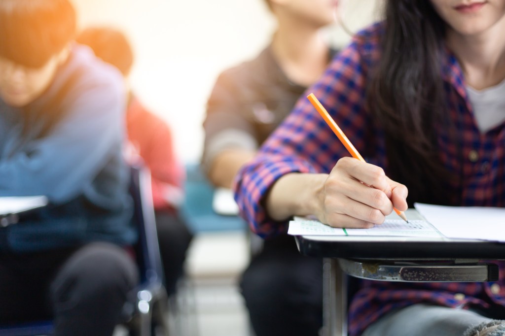 High school or university student sitting in lecture chair, writing on answer sheet for final exam, concept of scholarship for education abroad
