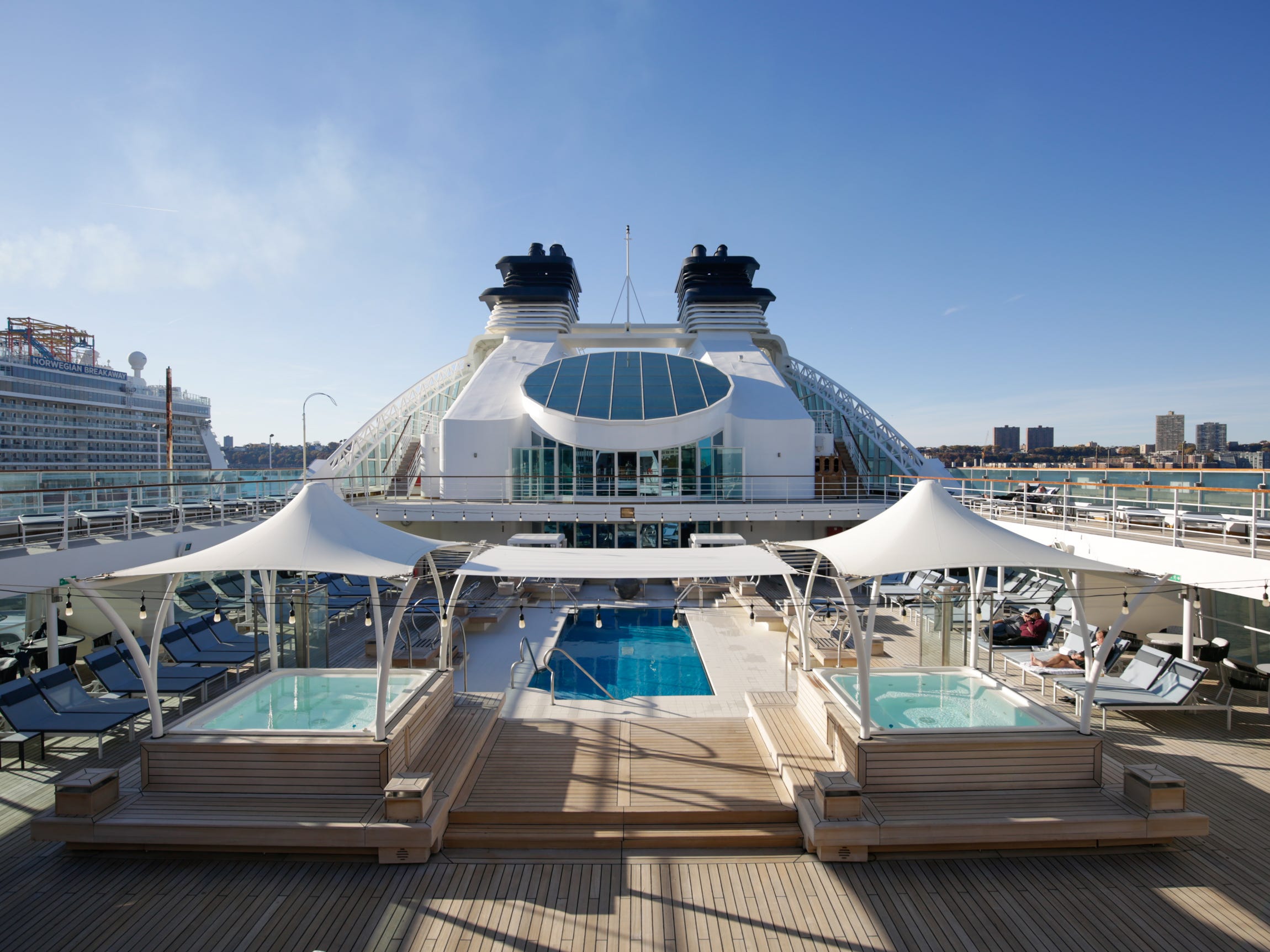 An empty pool deck of the Seabourn Quest cruise ship, featuring a larger pool in the center and two raised hot tubs on the sides.