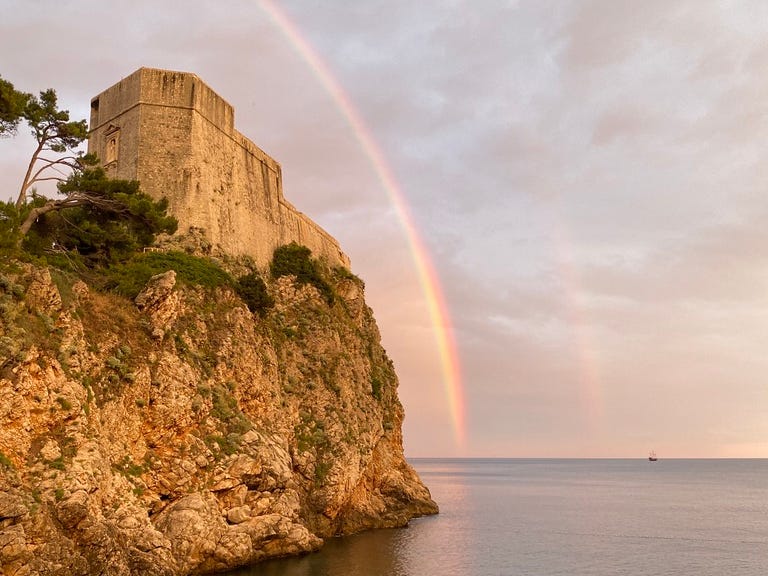 A rainbow over a fort on a cliff overlooking the sea.