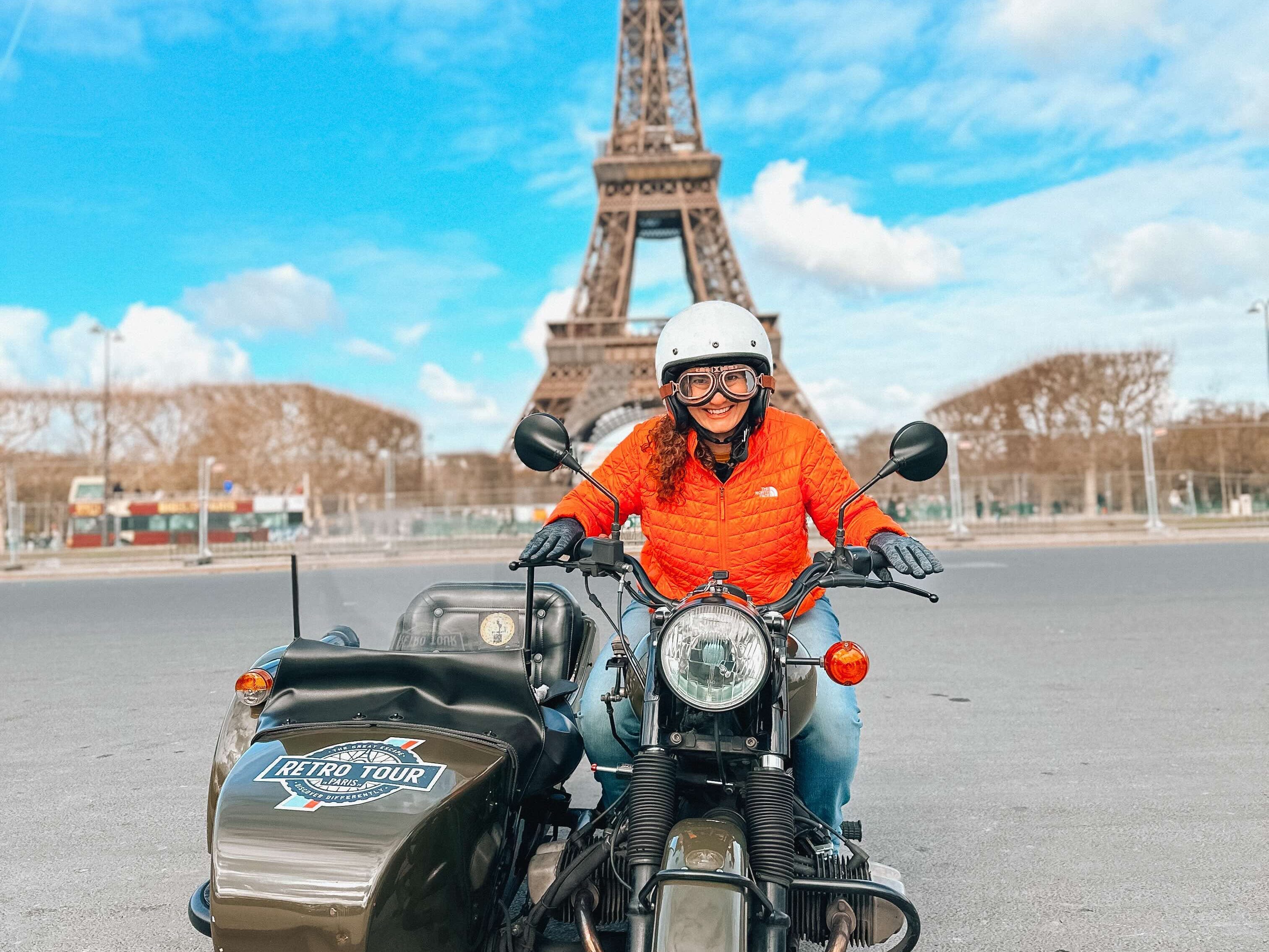 A woman in Paris on a motorcycle and sidecar, the Eiffel Tower in the background.