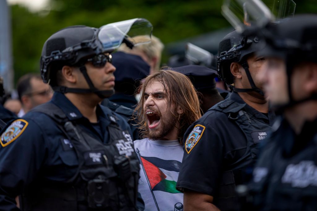 Handcuffed protester shouting at law enforcement during a student-led pro-Palestine demonstration at Brooklyn College, New York, with NYPD officers in the background after an arrest.