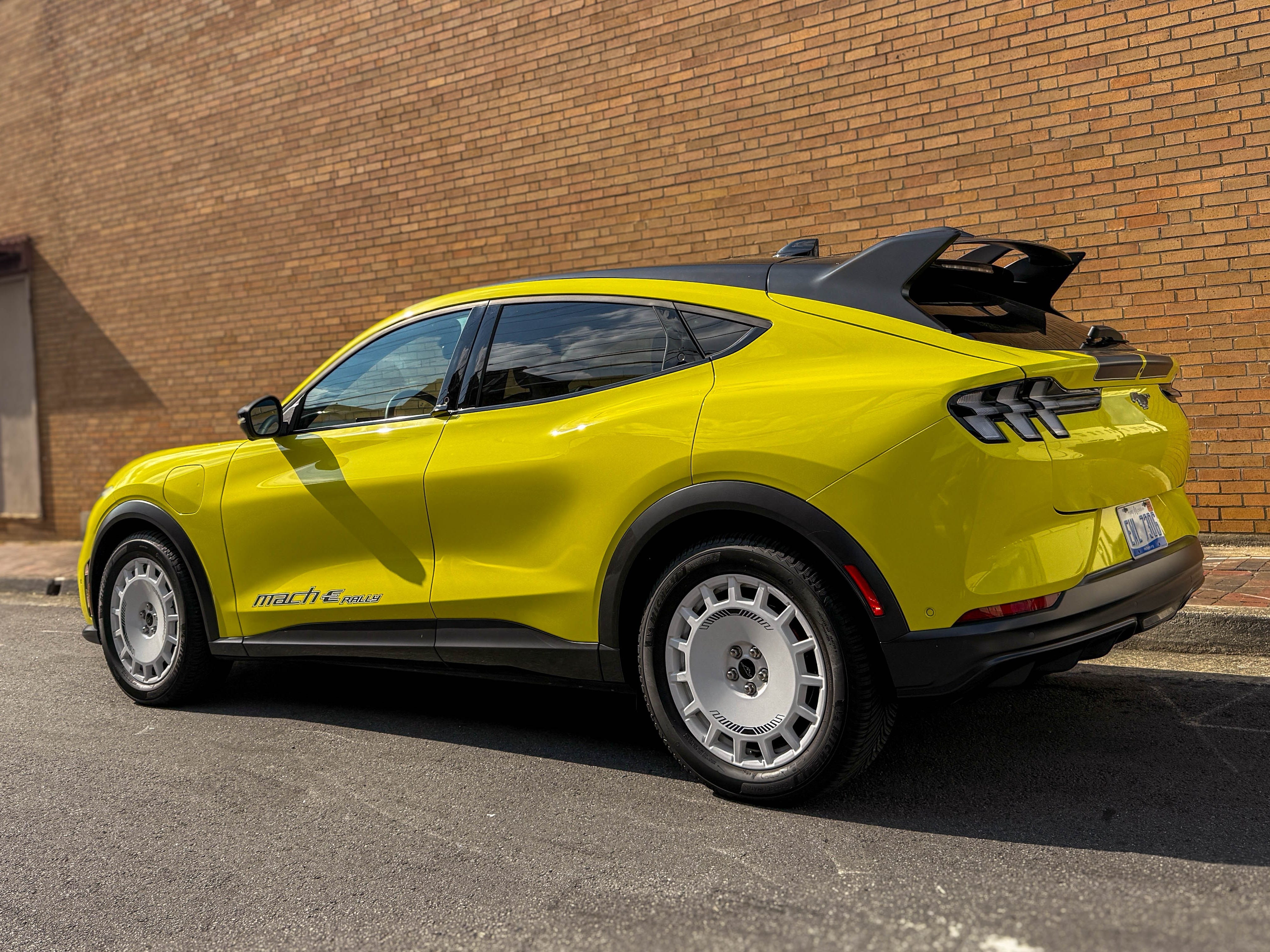 The left rear of a yellow 2025 Ford Mustang Mach-E Rally EV SUV parked on the street.