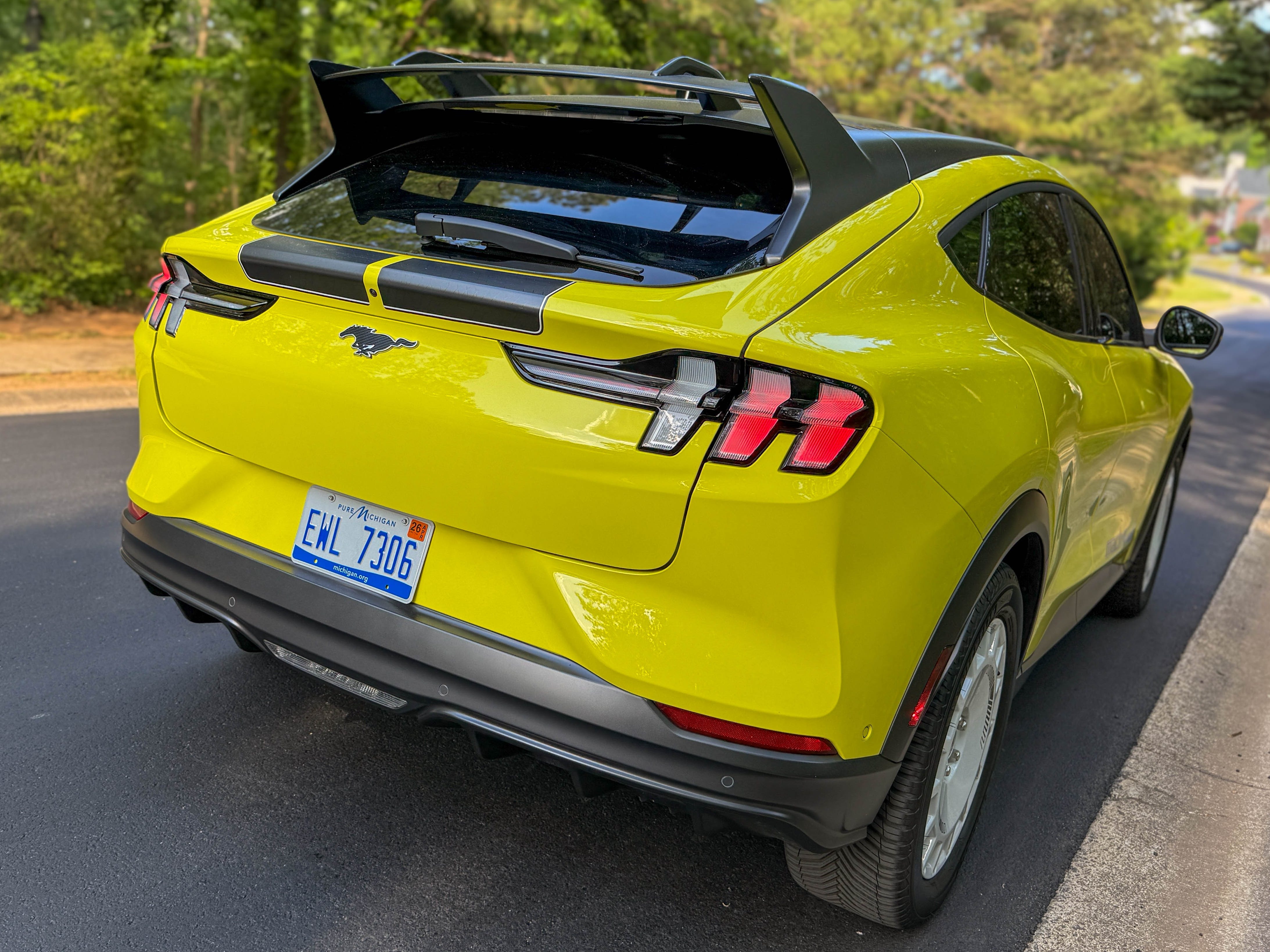 The right rear of a yellow 2025 Ford Mustang Mach-E Rally EV SUV parked by the woods.